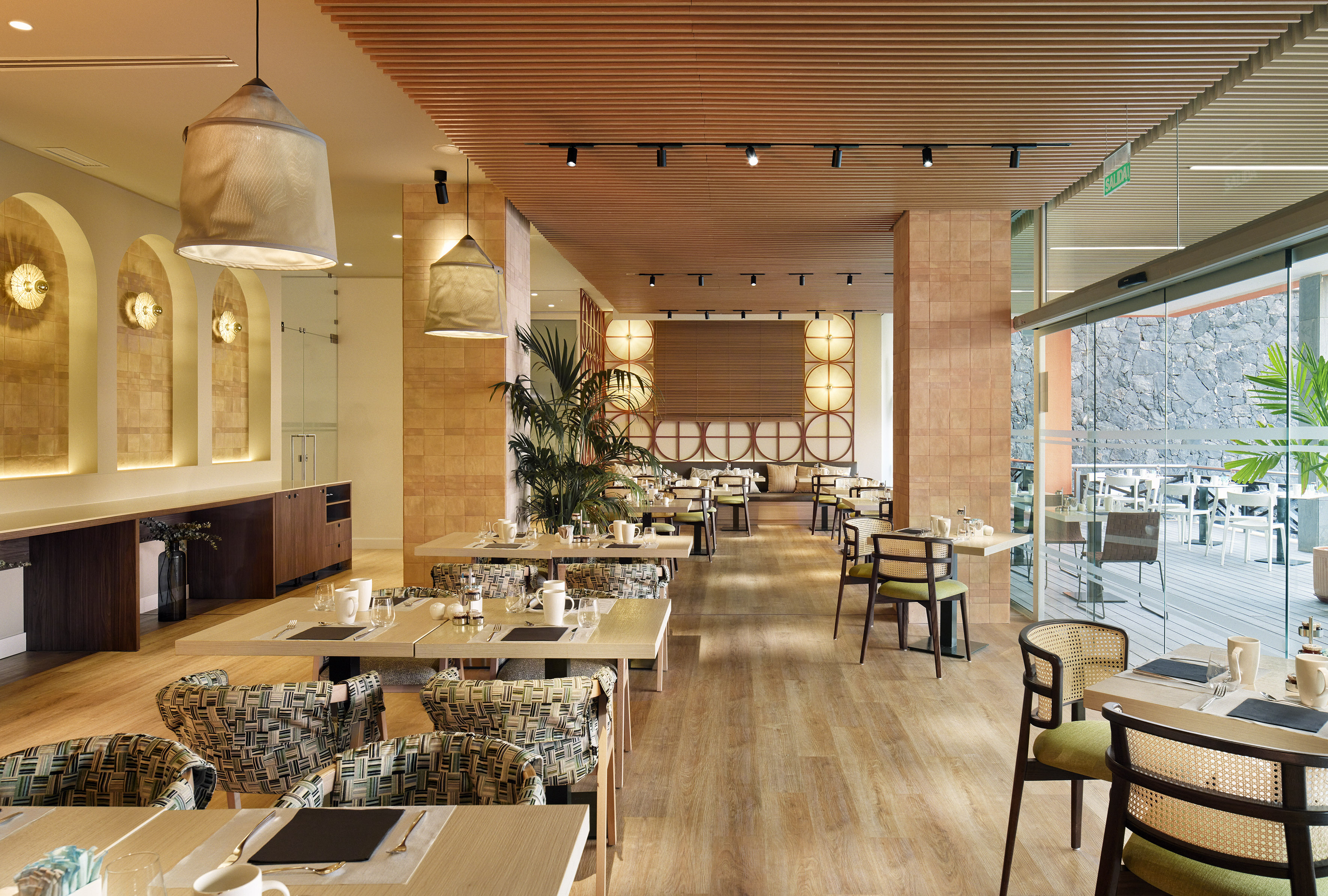 Contemporary restaurant with wooden ceiling, set tables, outdoor patio view.