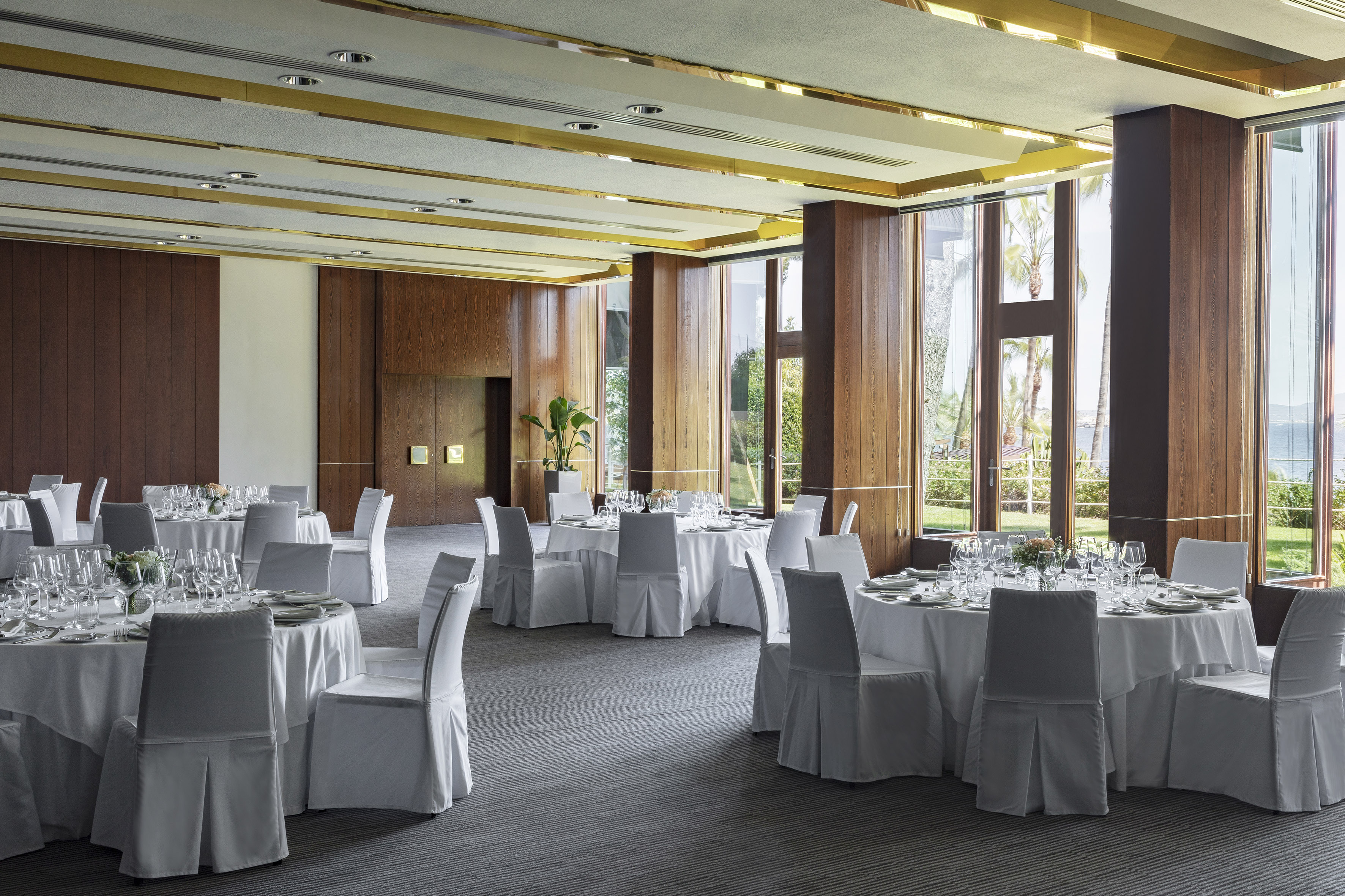 Bright ballroom with set tables, wood walls, and large windows with sea view.