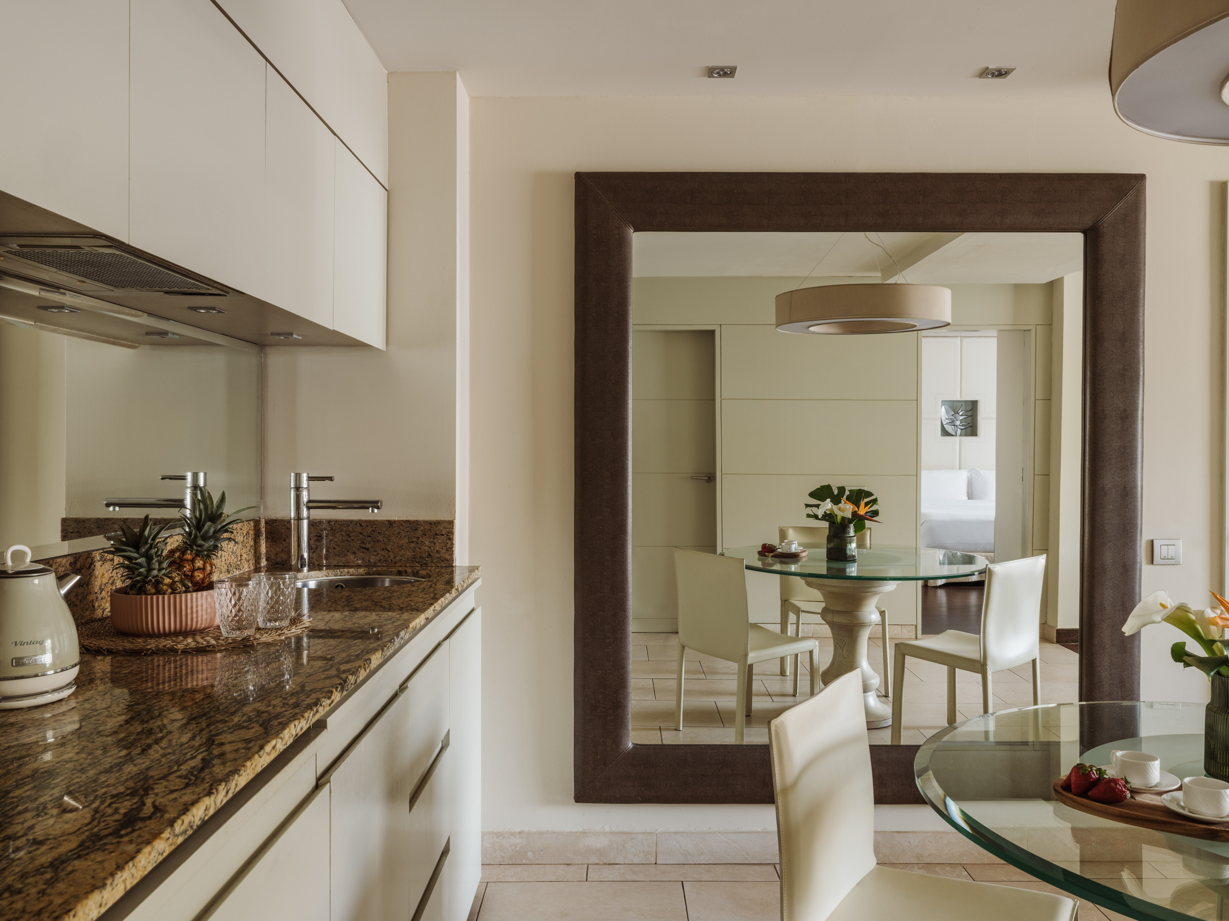 Modern kitchen with granite counter, mirror reflecting dining area and bedroom.