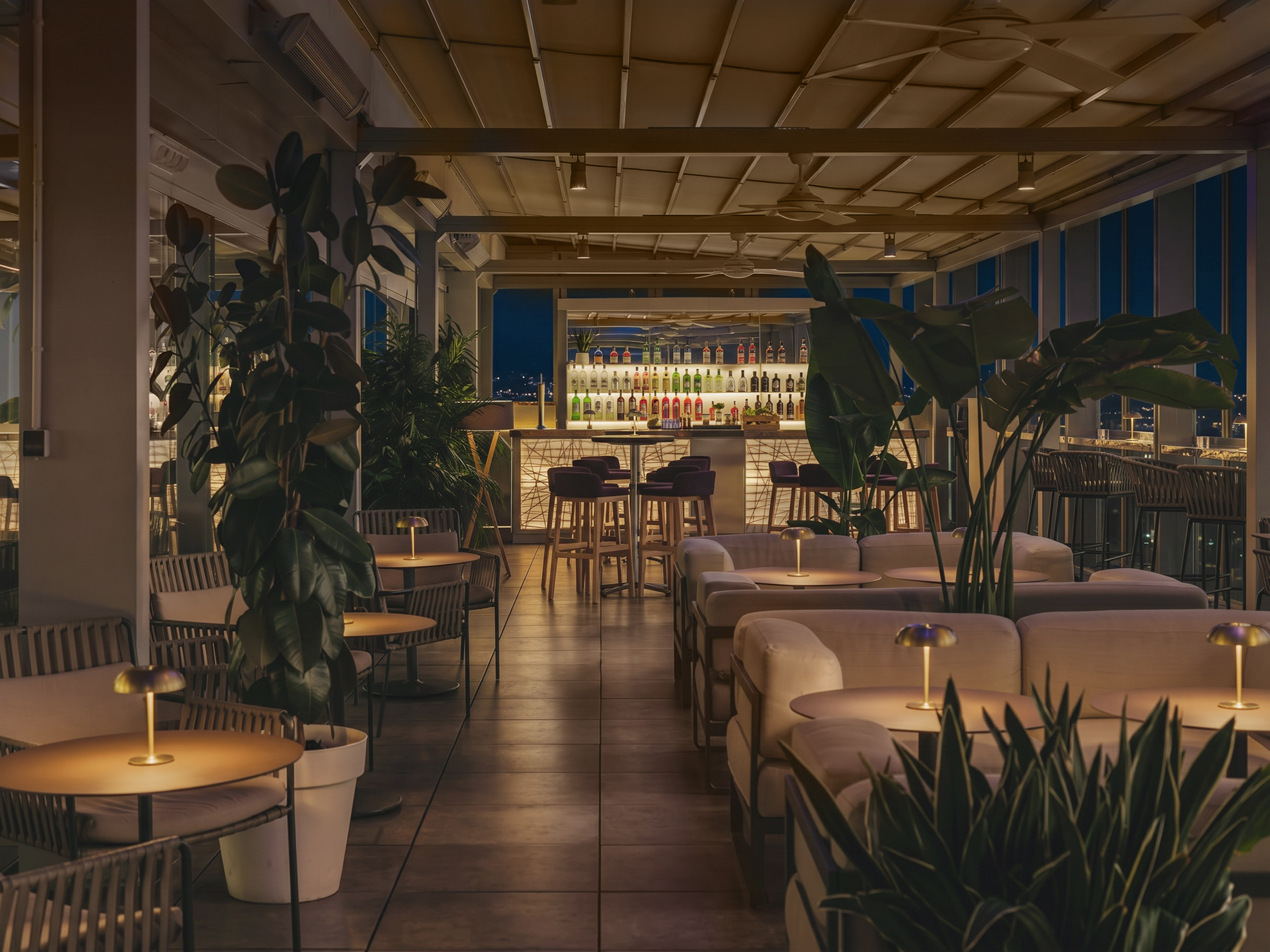 Elegant rooftop lounge bar at night with illuminated bottles and lush plants.