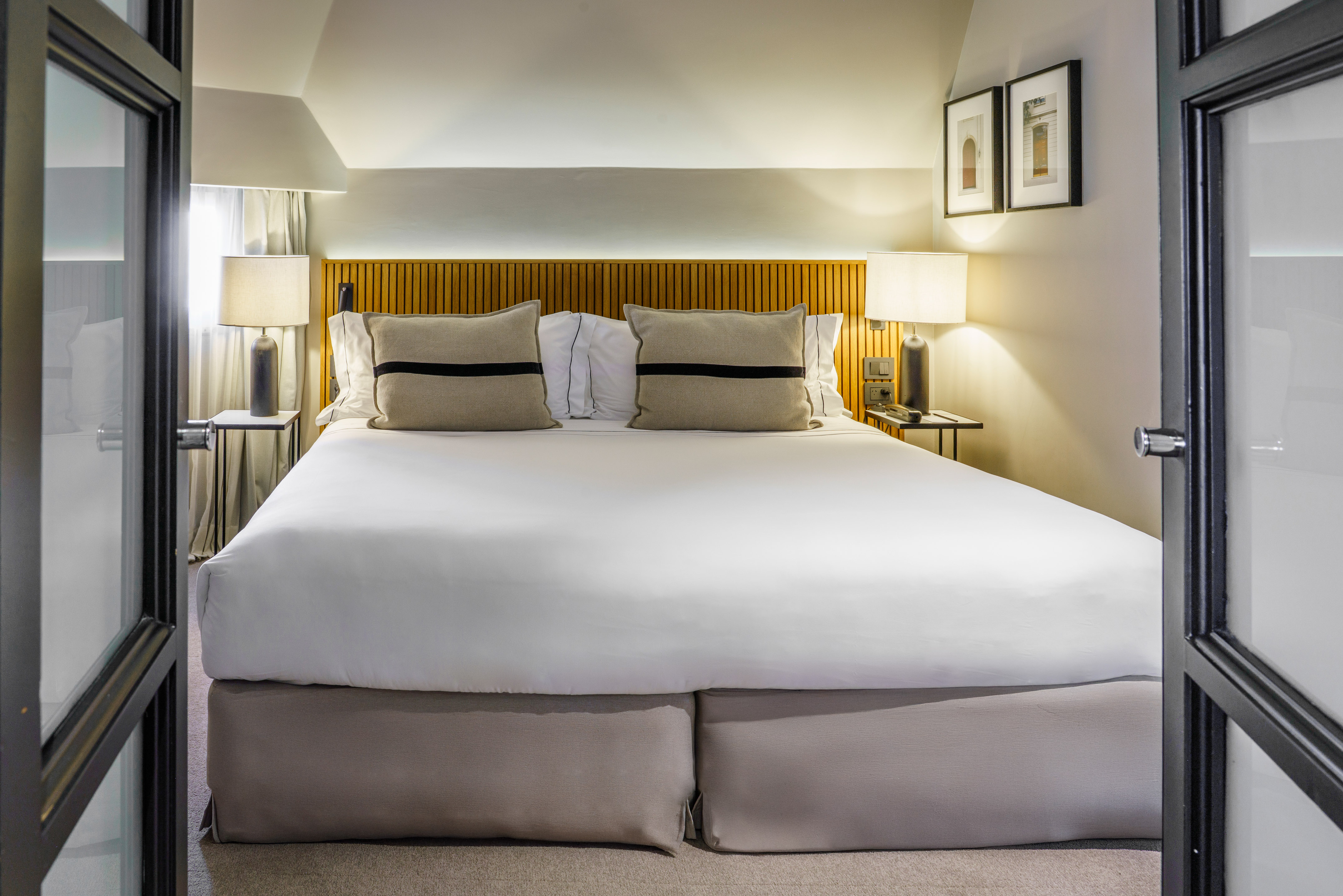 Hotel bedroom with a large bed, modern wood headboard, and bedside lamps.