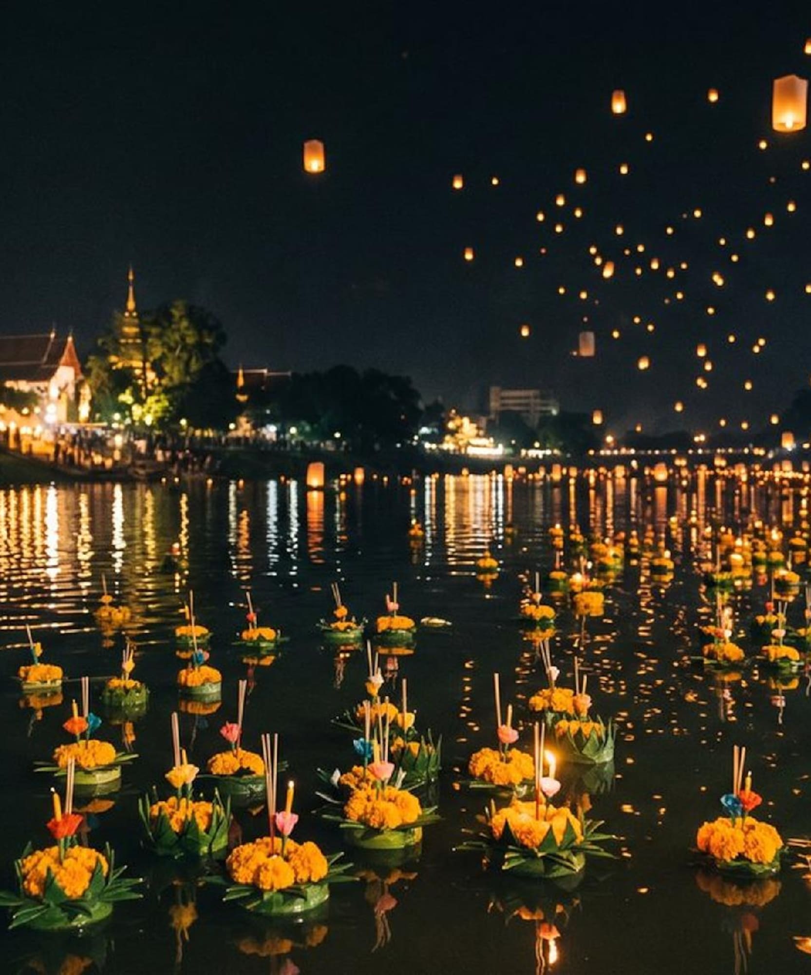 Loy Krathong festival: krathongs on river, sky lanterns illuminate night.