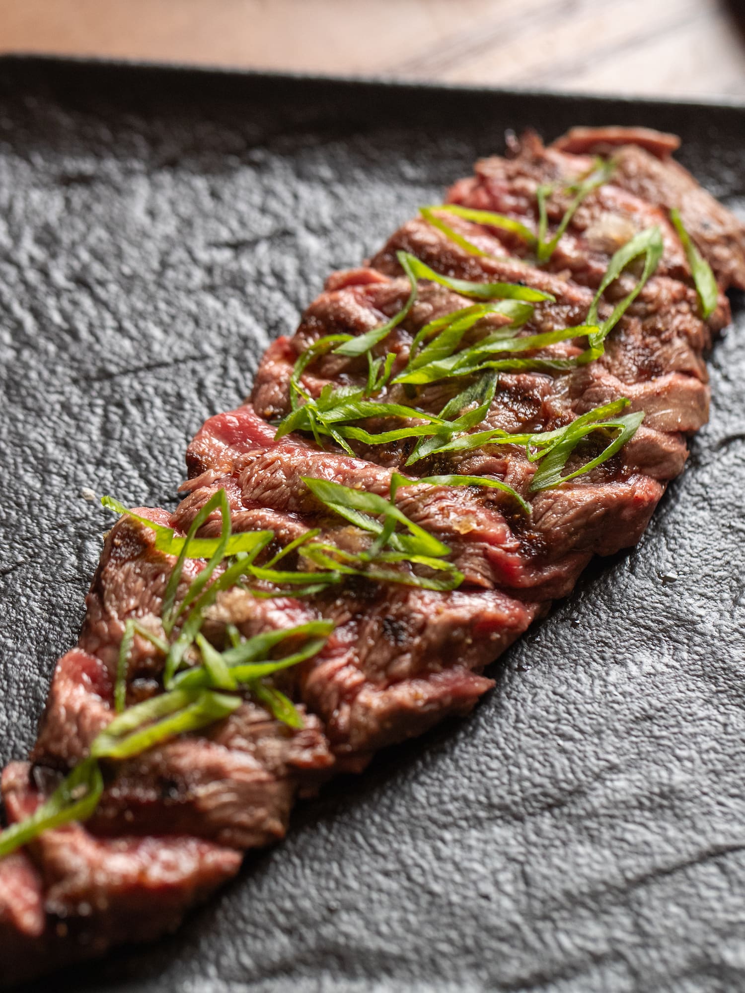 a piece of meat with green garnish on a black plate