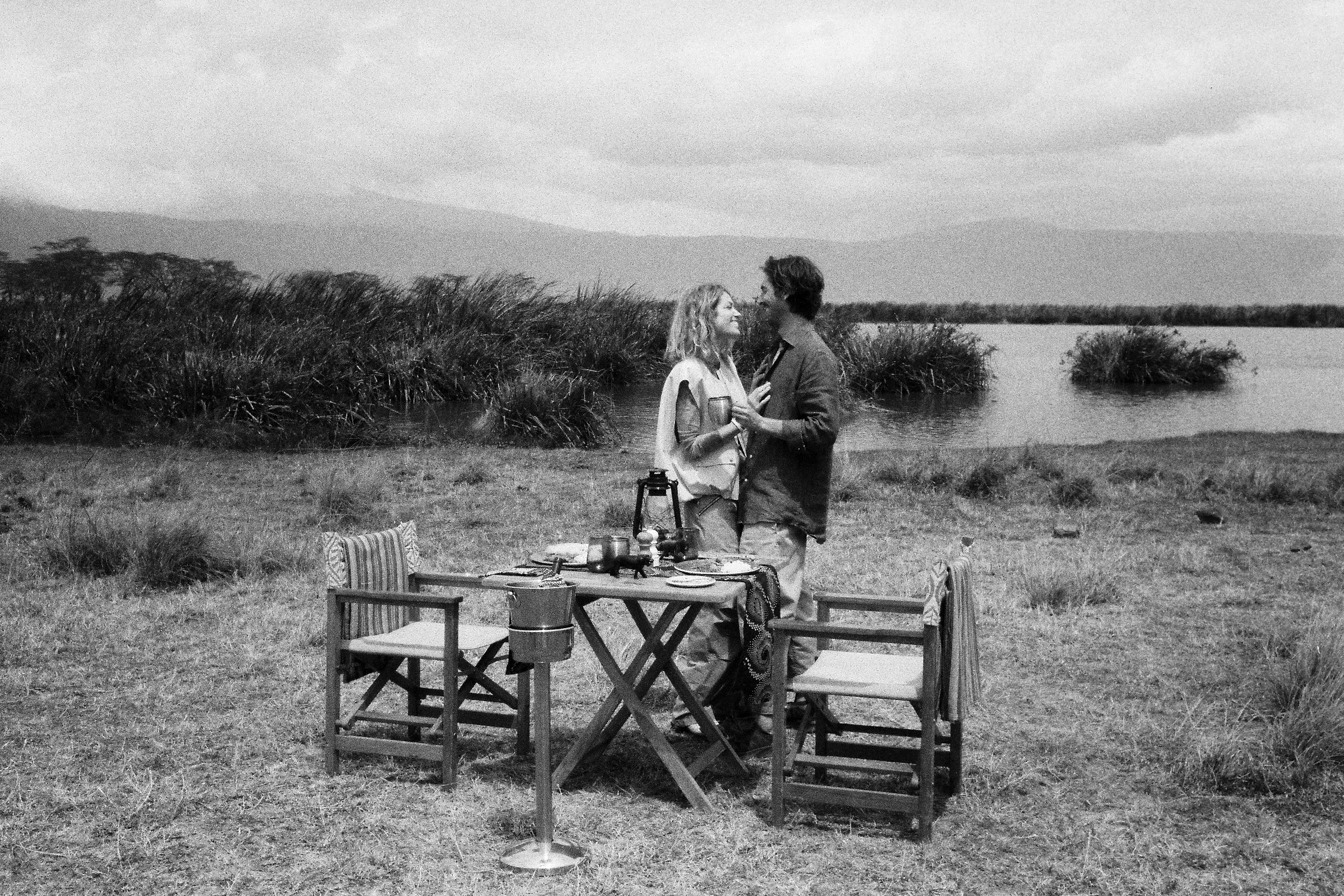 Couple enjoys private outdoor dining by lake, African safari setting.