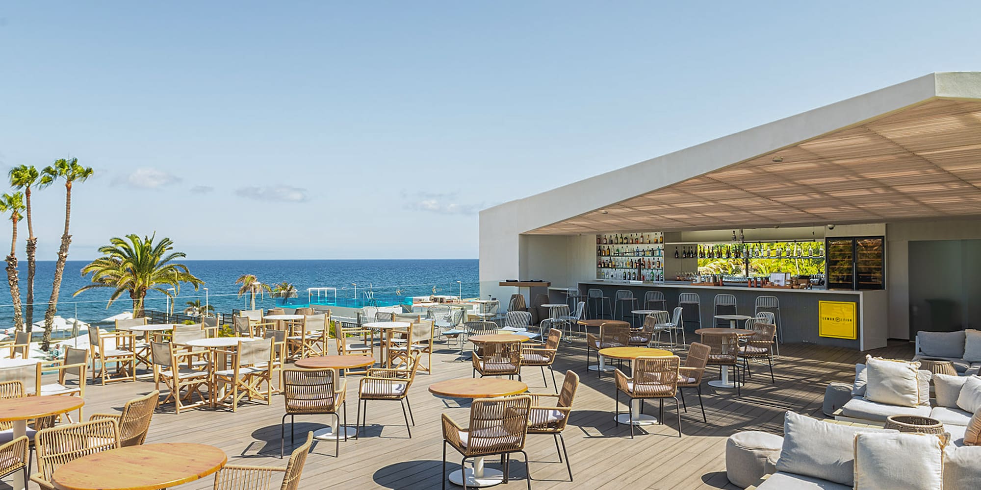 a patio with tables and chairs on a deck overlooking the ocean