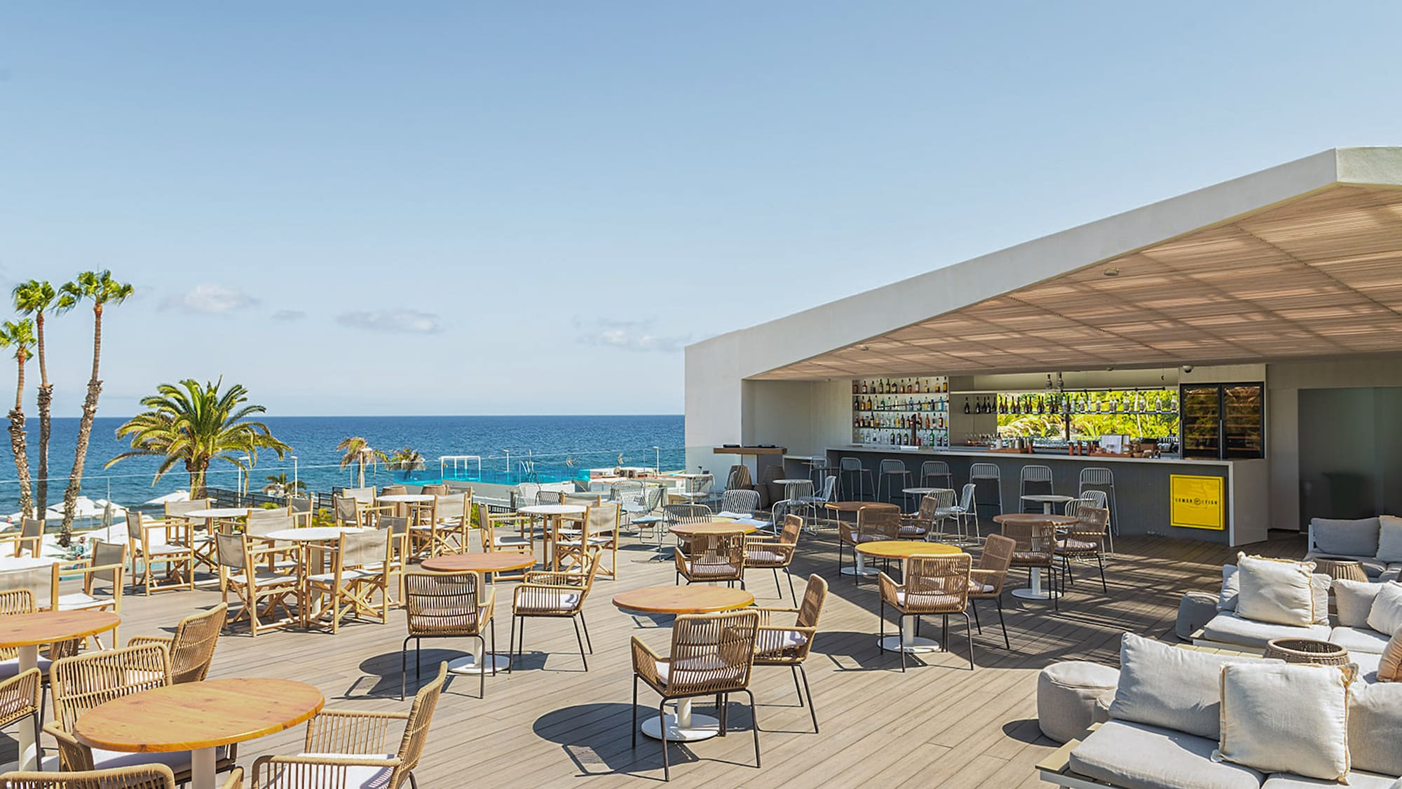 a patio with tables and chairs on a deck overlooking the ocean