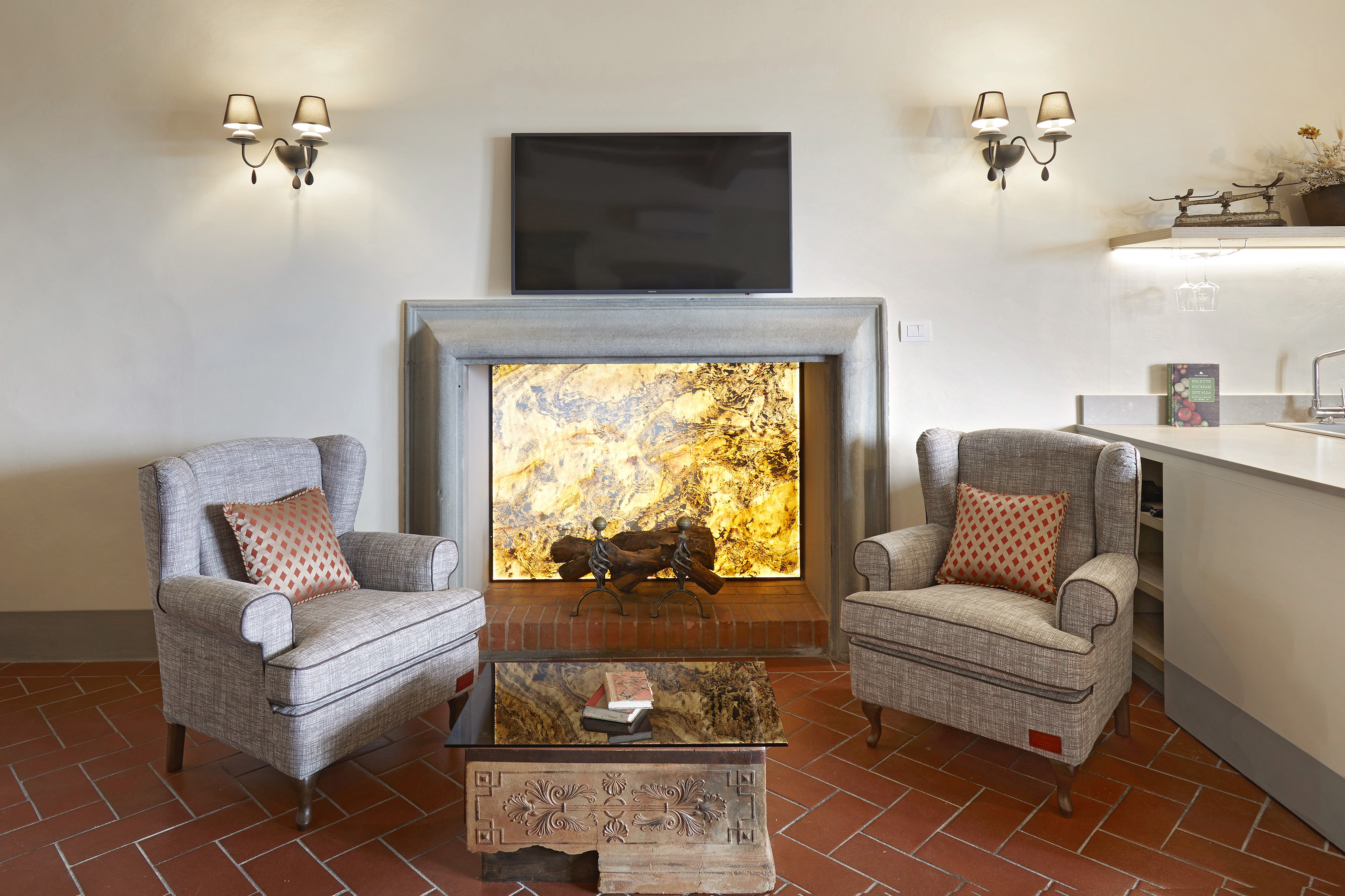 Living room with two armchairs, illuminated fireplace, TV, and terracotta floor.