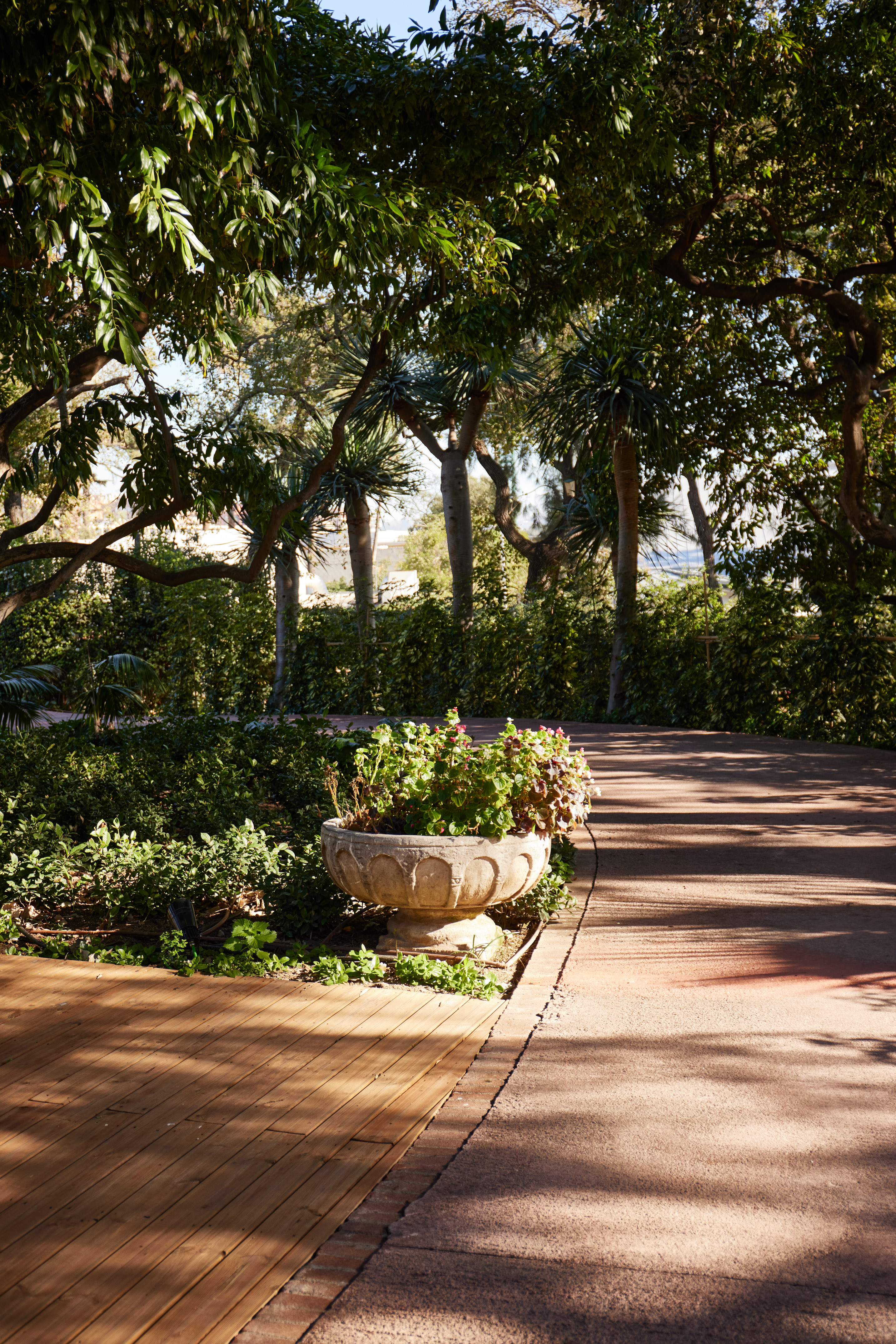 Lush garden with stone planter, trees, wooden deck, and shaded pathway.