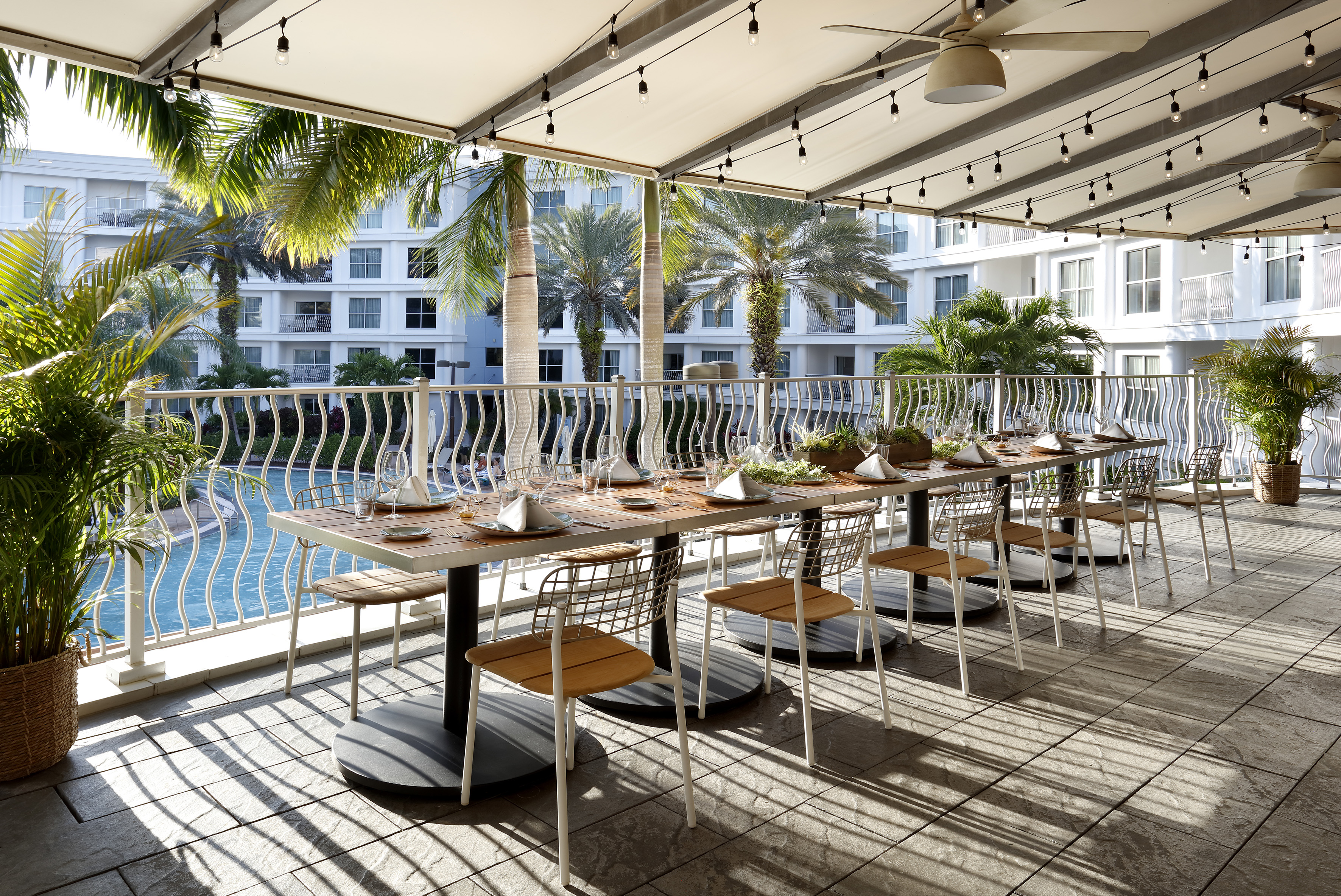 Modern resort outdoor dining patio with tables set by pool and palm trees. - The Pearl (circular floor plan) - Meliá Orlando Celebration, Orlando