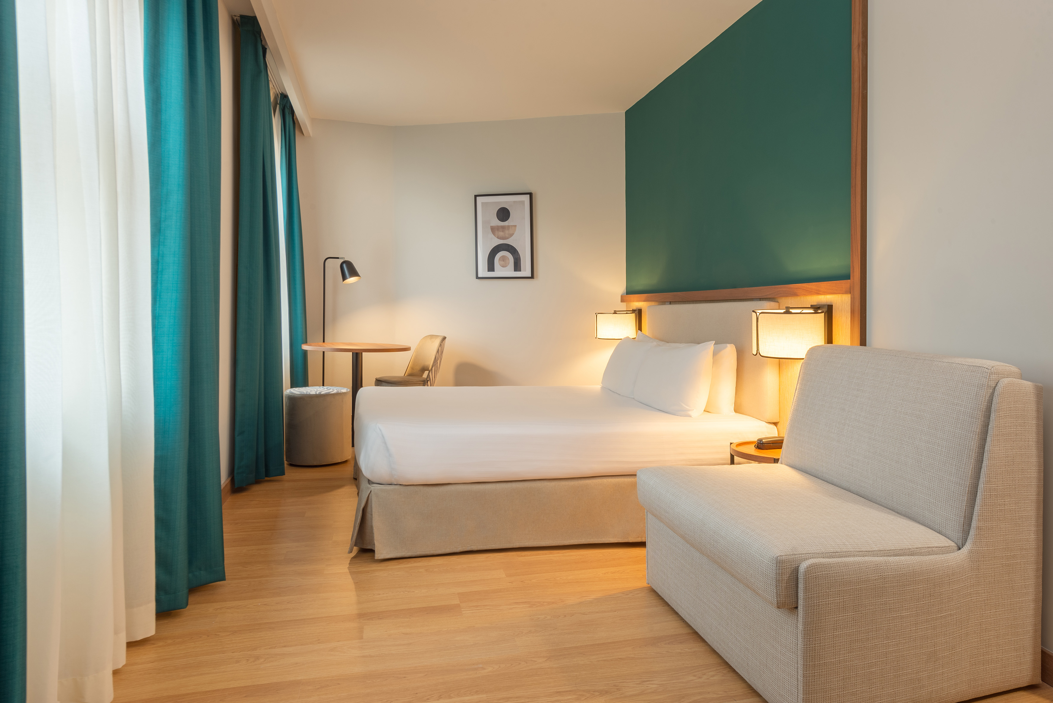 Modern hotel bedroom with white bed, green accent wall, and teal curtains.