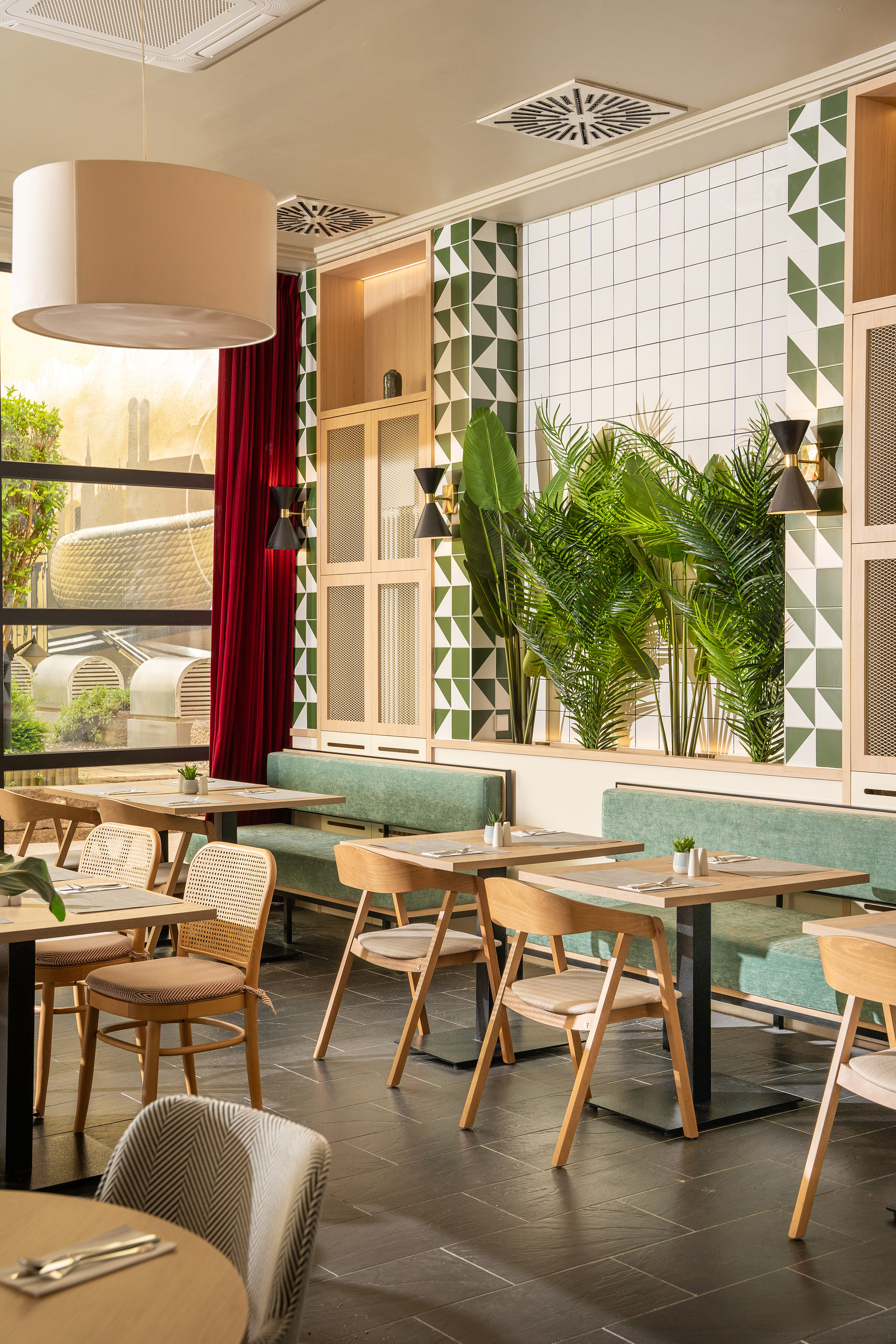 Modern dining area with green tile walls, light wood furniture, and tropical plants.