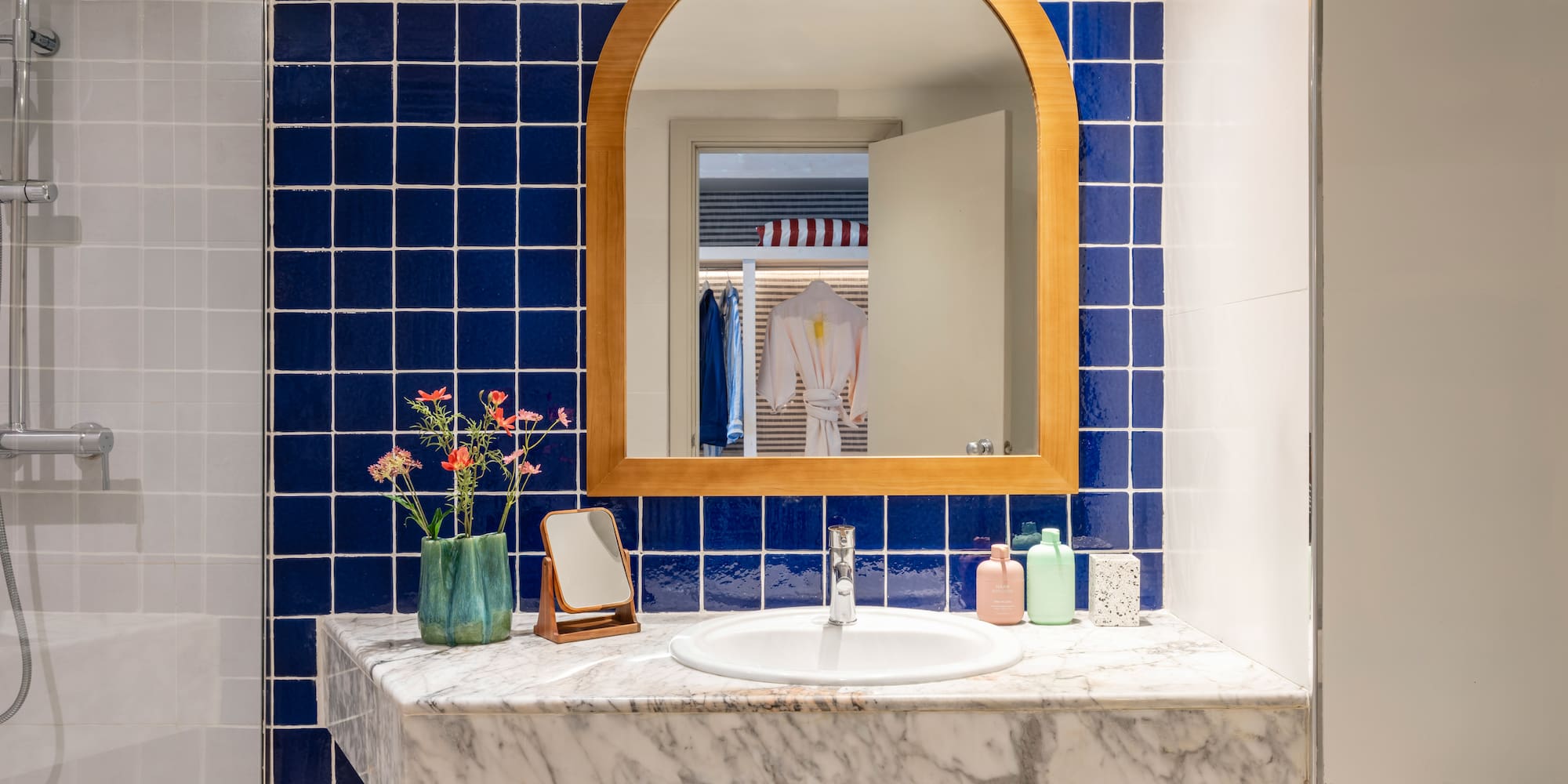 Baño moderno con azulejos azules, encimera de mármol y espejo arqueado.