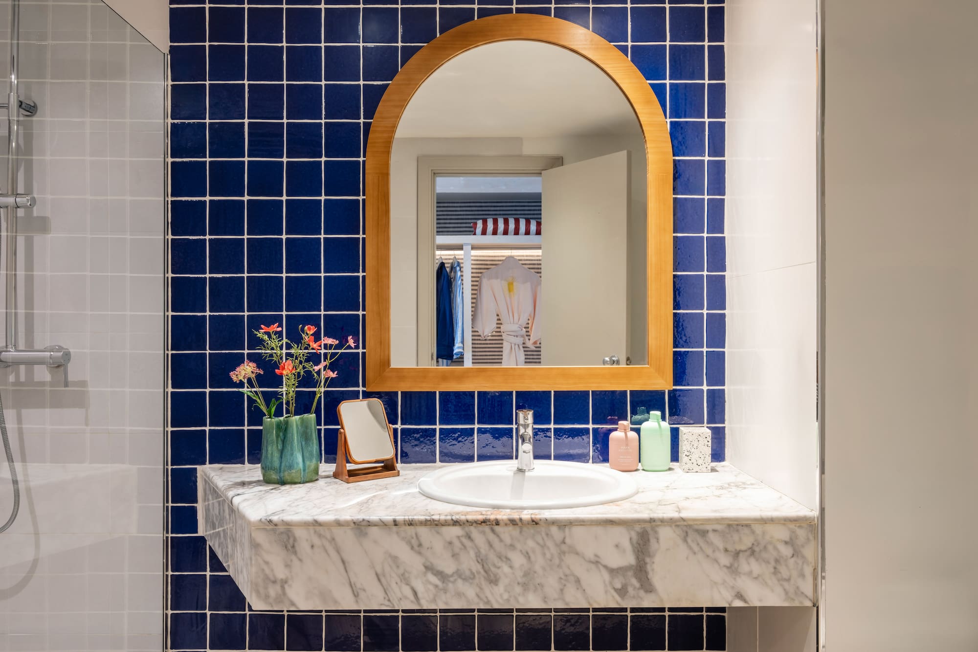 Baño moderno con azulejos azules, espejo arqueado de madera y lavabo de mármol.