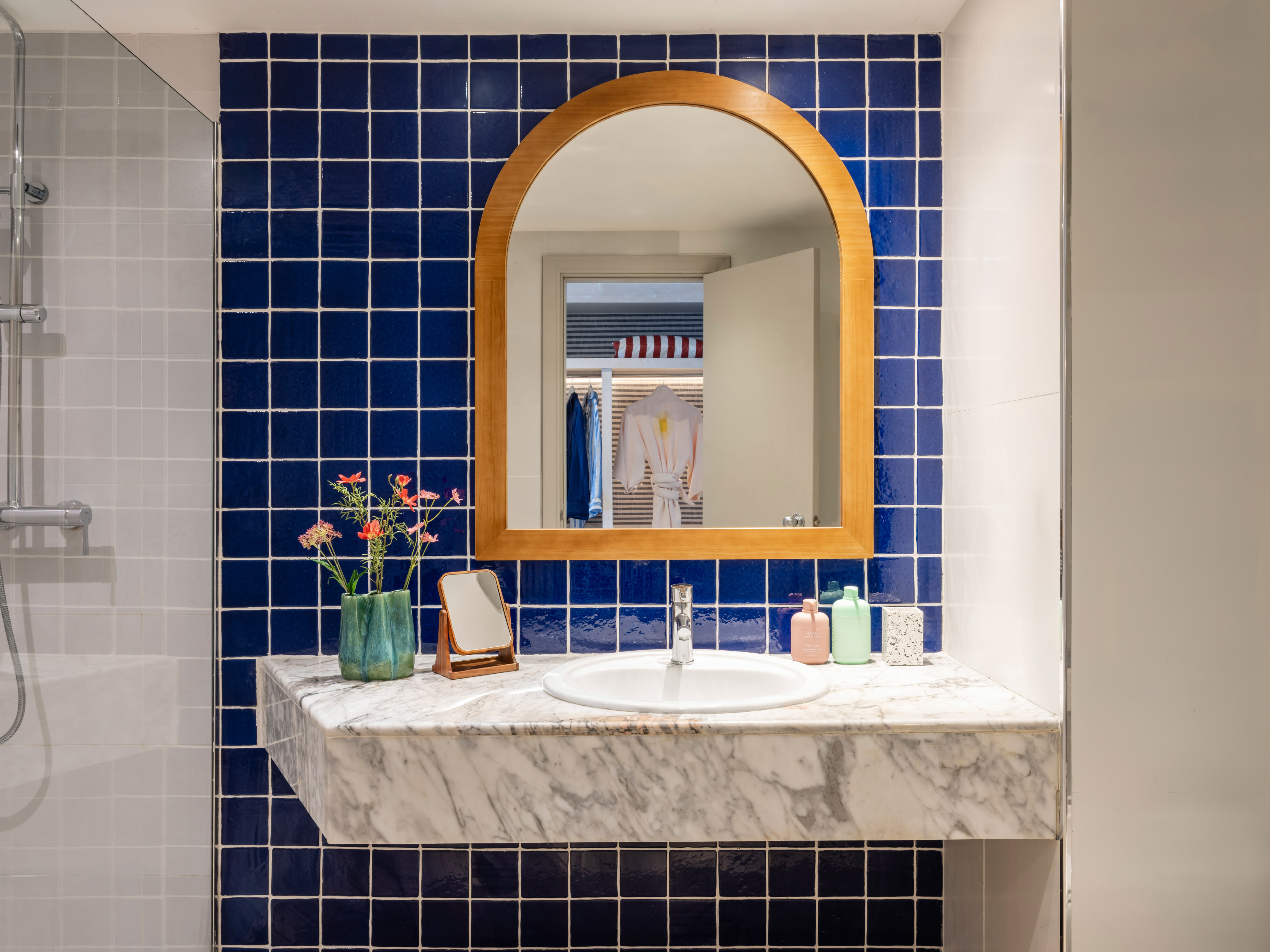 Baño moderno con azulejos azules, espejo arqueado de madera y lavabo de mármol.