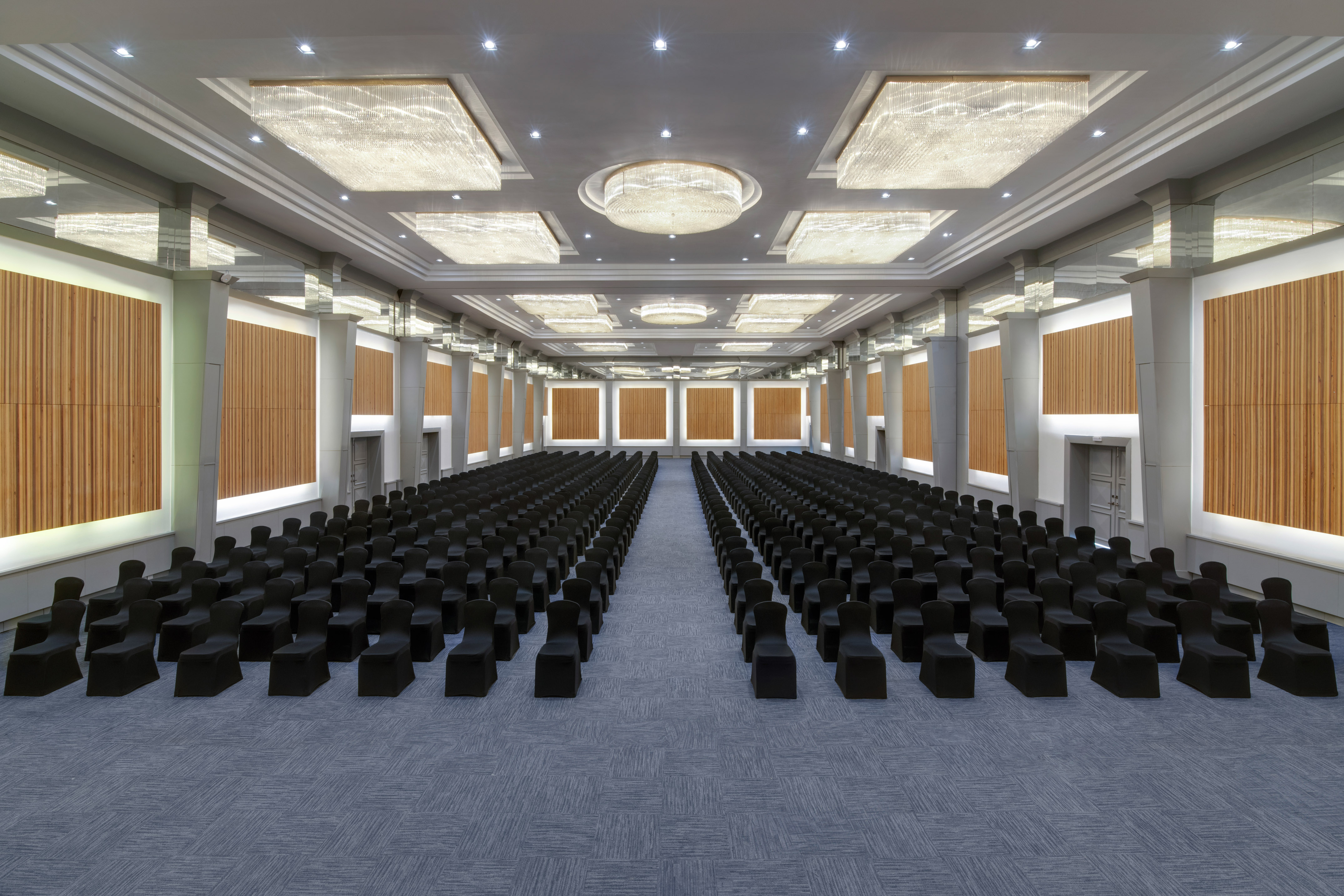 Empty luxury ballroom with black chairs, wood panels, and crystal chandeliers.