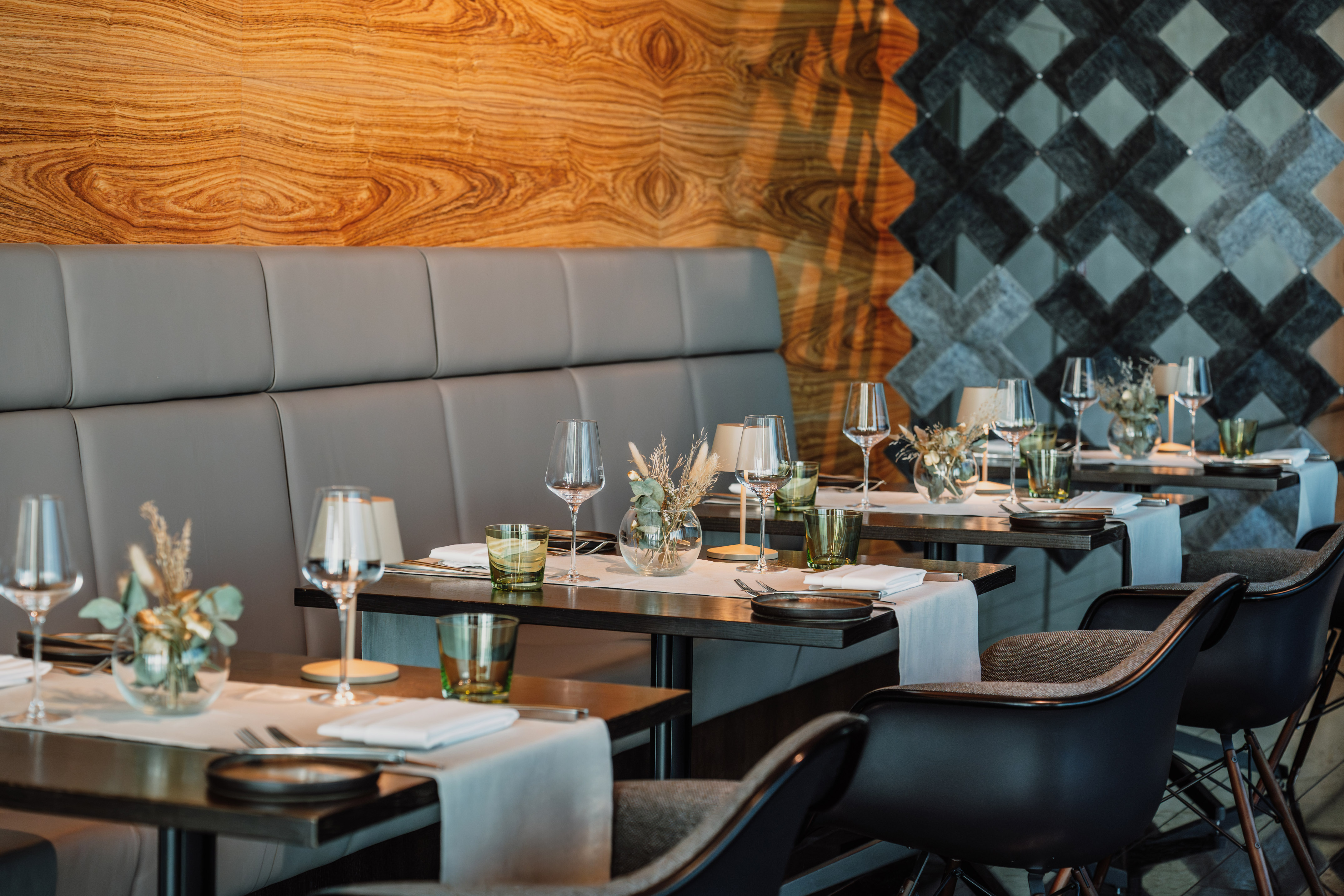 Modern restaurant dining room with set tables, wooden walls, and booth seating.
