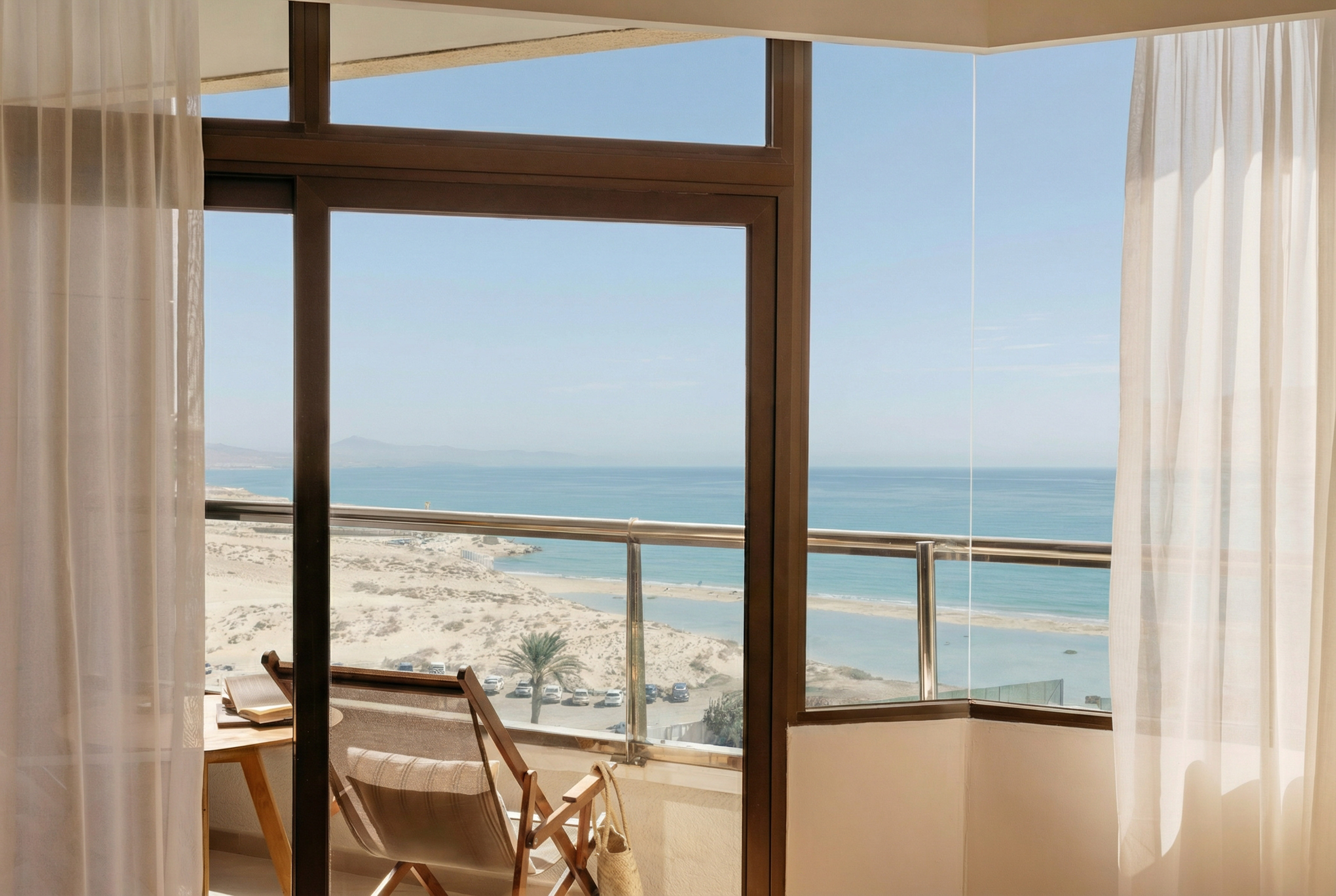 Hotel room balcony overlooking sandy beach and blue ocean.