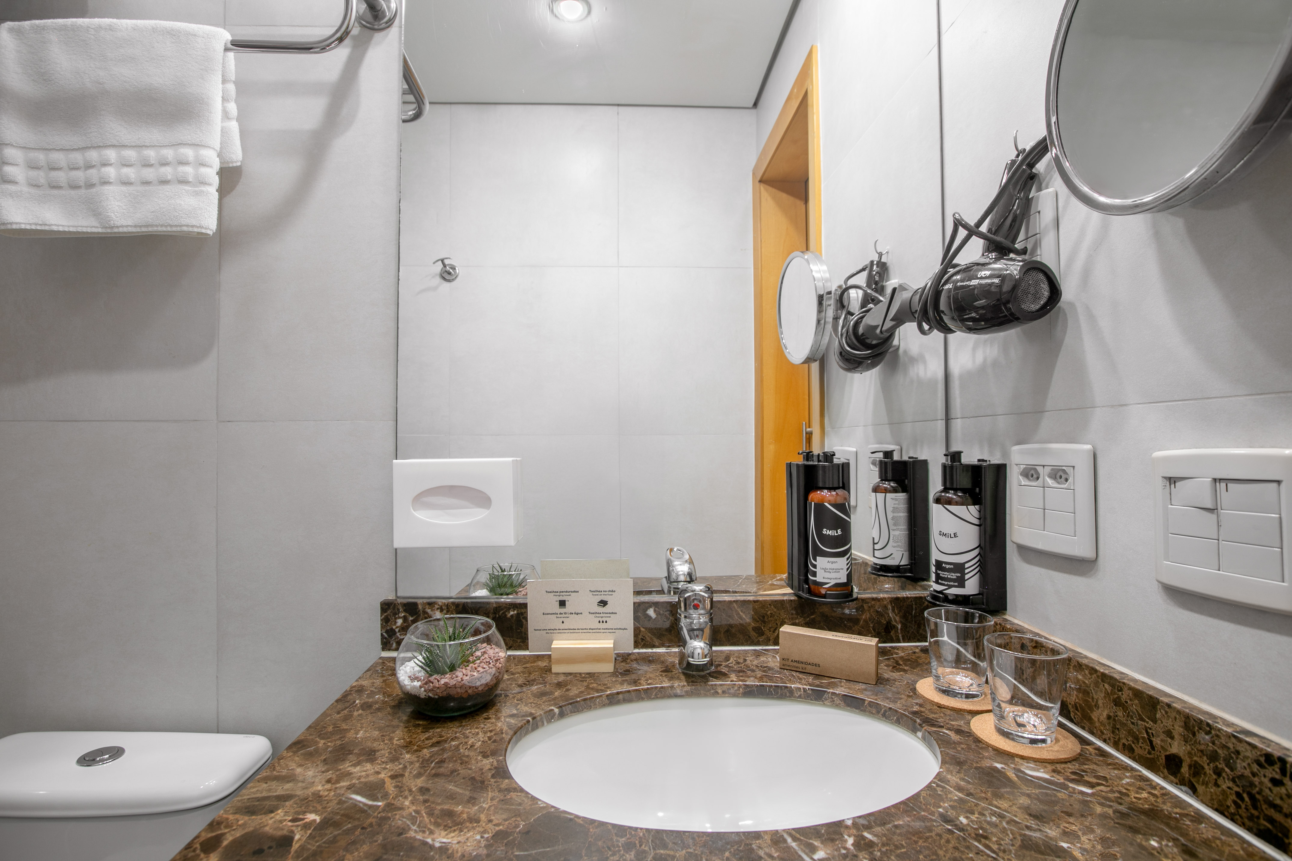 Modern bathroom vanity with marble top, sink, hairdryer, toiletries, white towels.