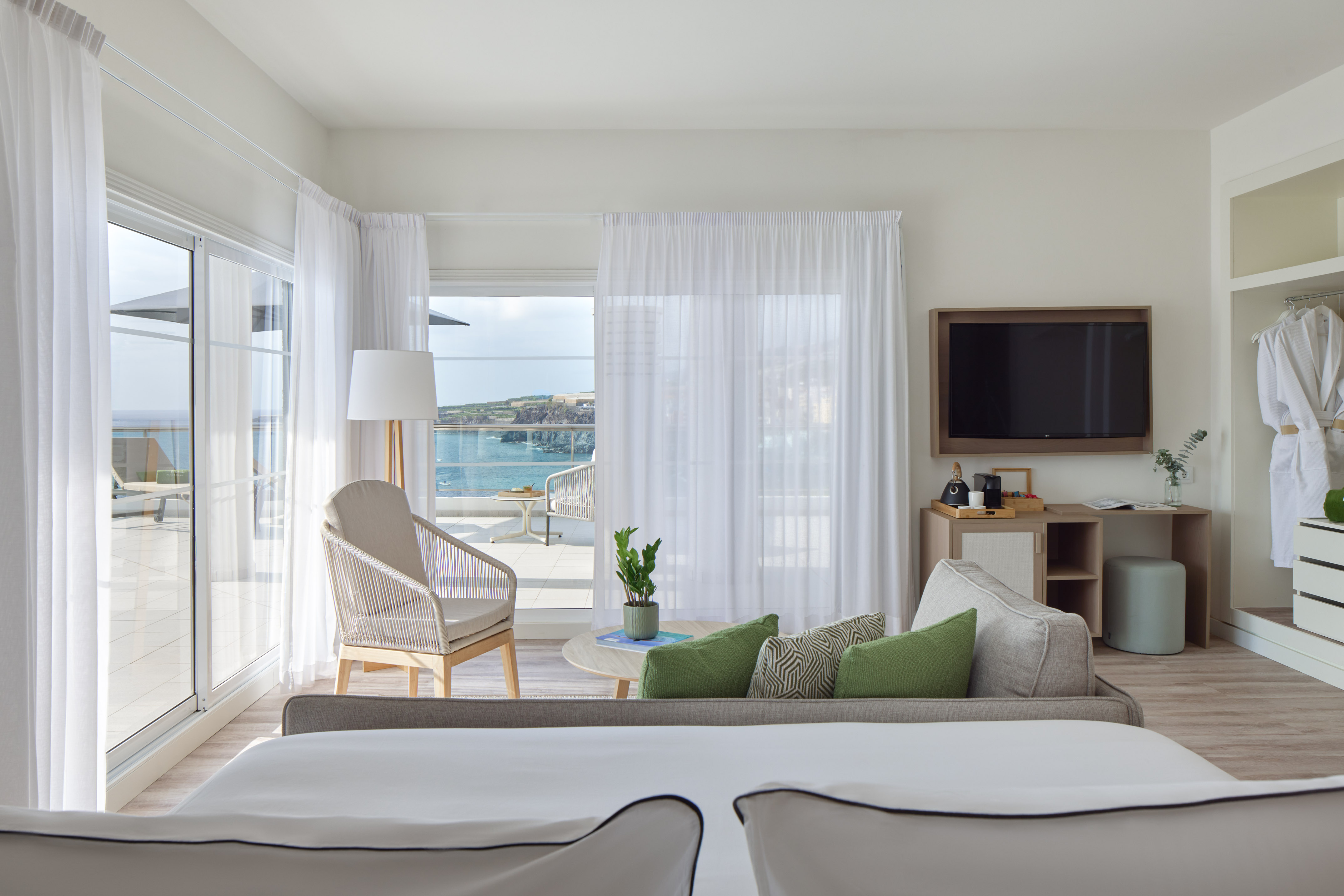 Modern hotel suite with ocean view balcony, sofa, bed, and flat-screen TV.