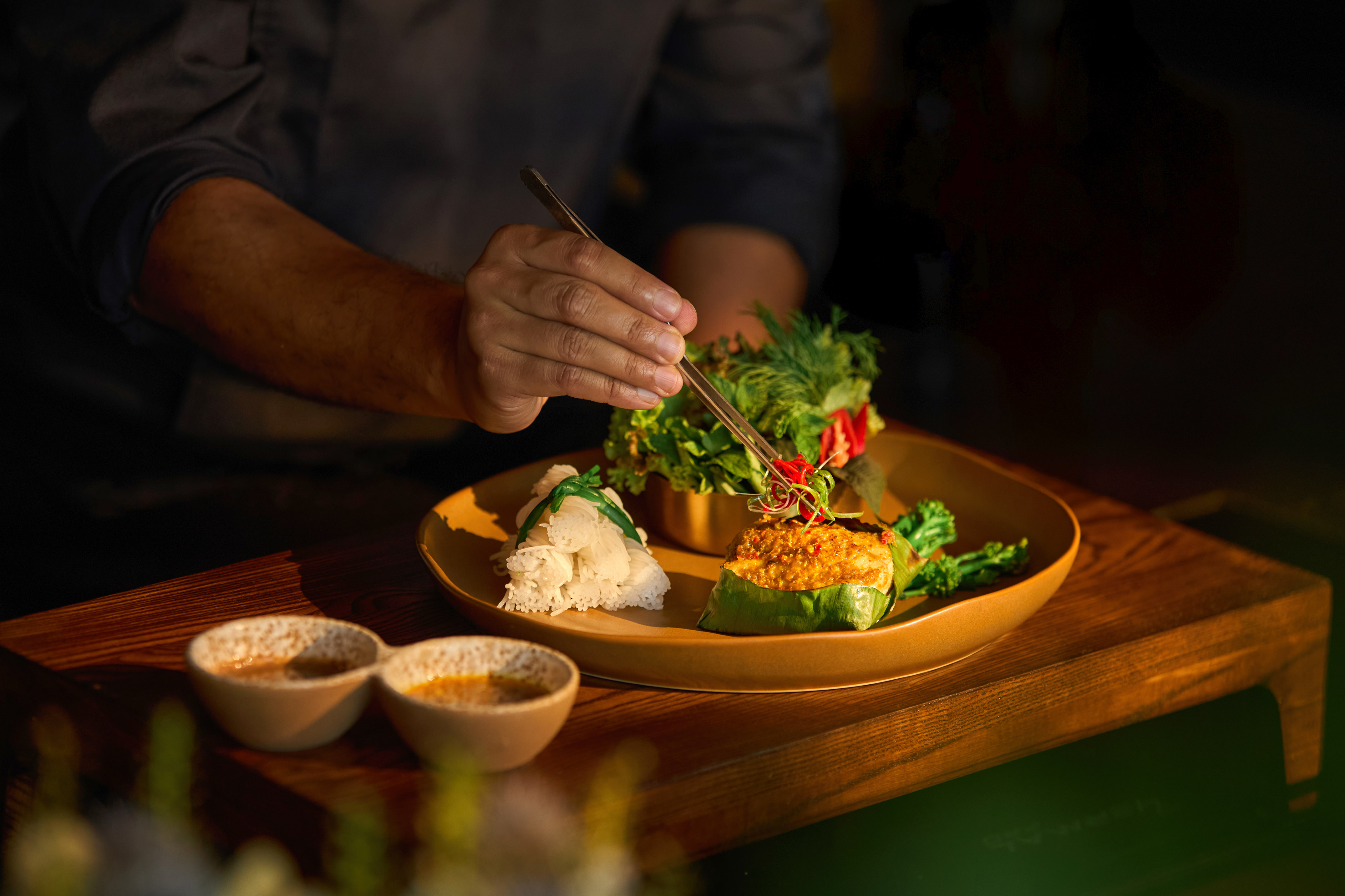 Chef carefully plating gourmet curry dish with rice noodles and fresh greens.