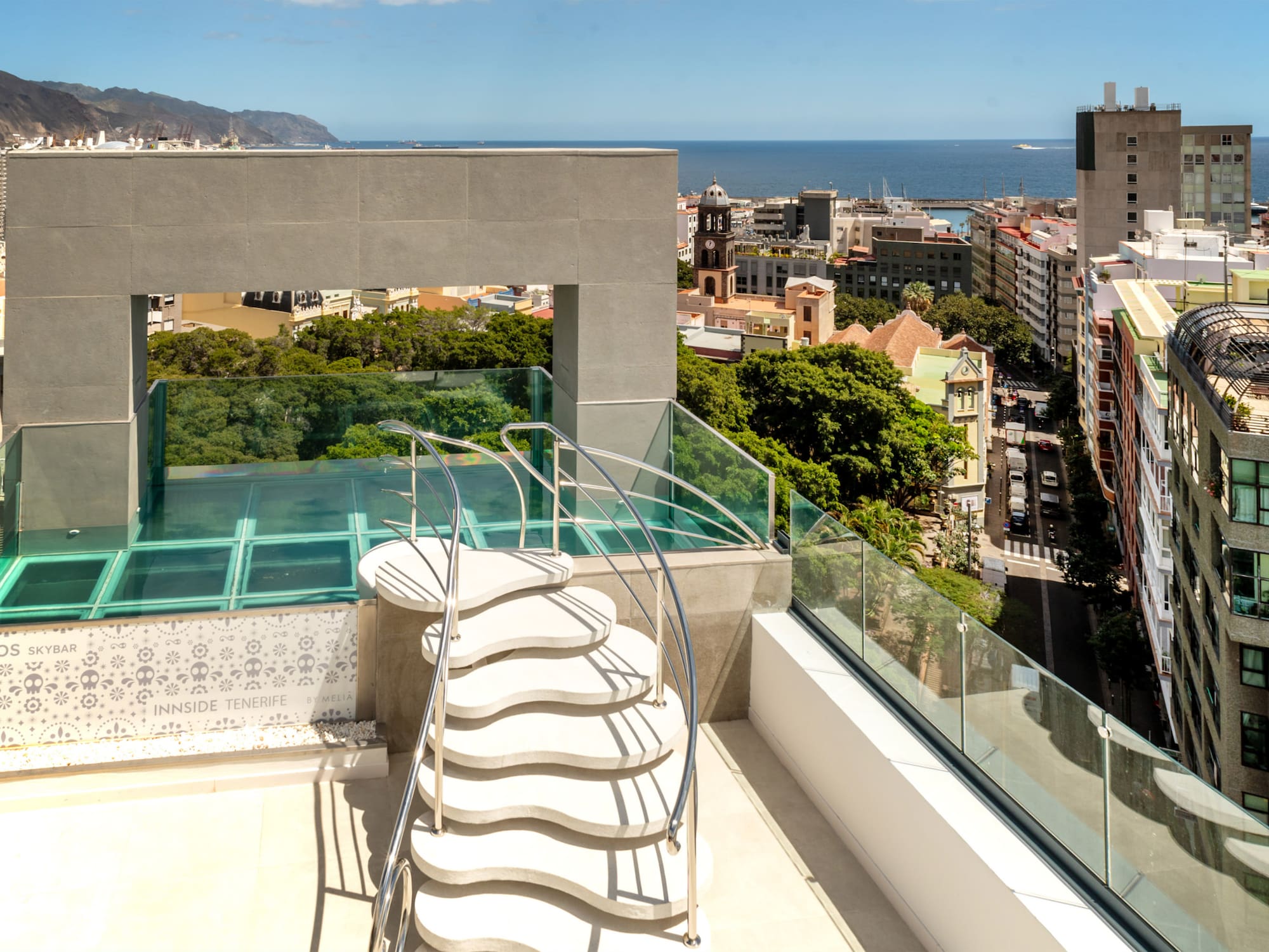 Tenerife skybar rooftop: wavy stairs, glass floor, city, and ocean view.