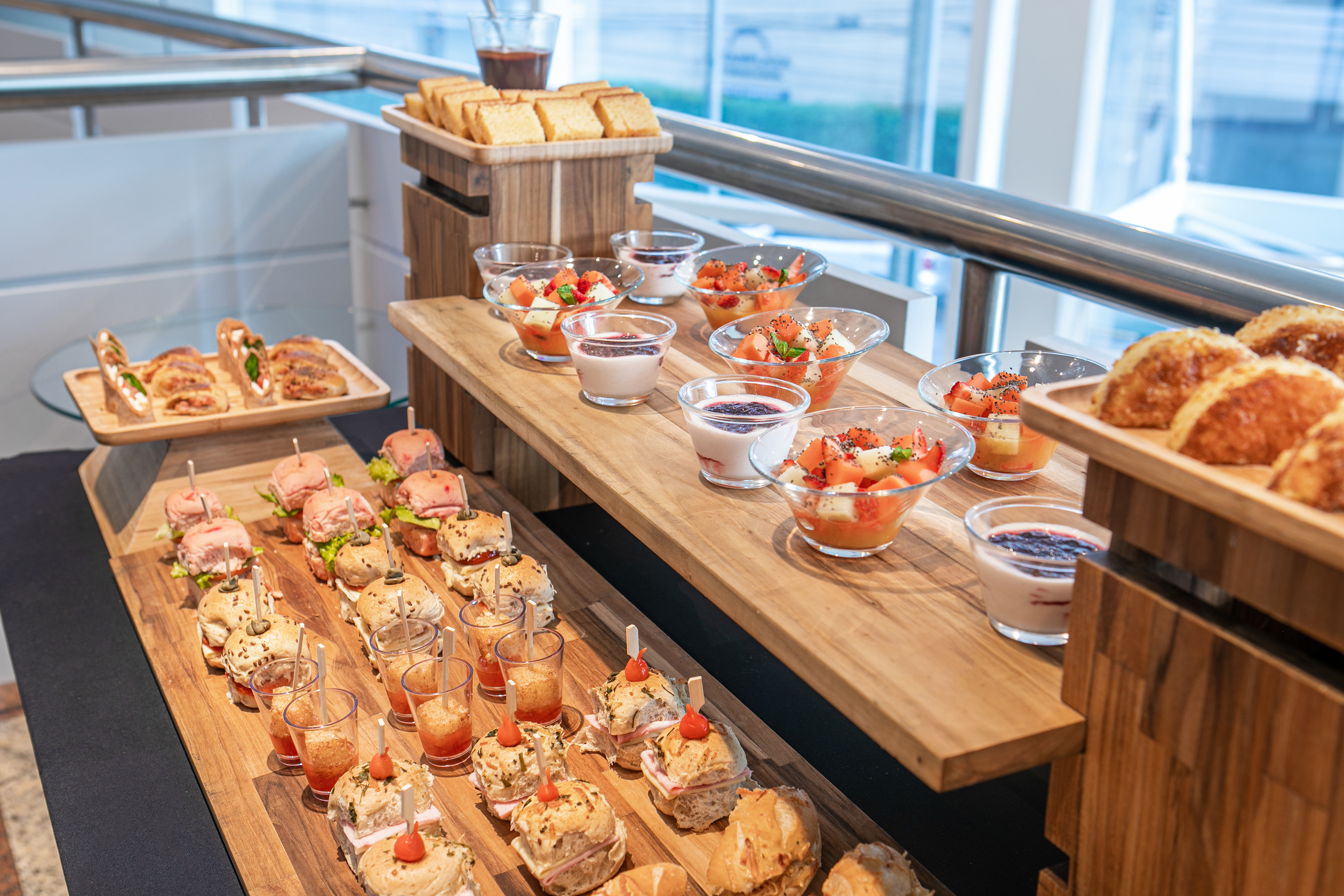 Event catering buffet with mini sandwiches, fruit cups, and desserts.