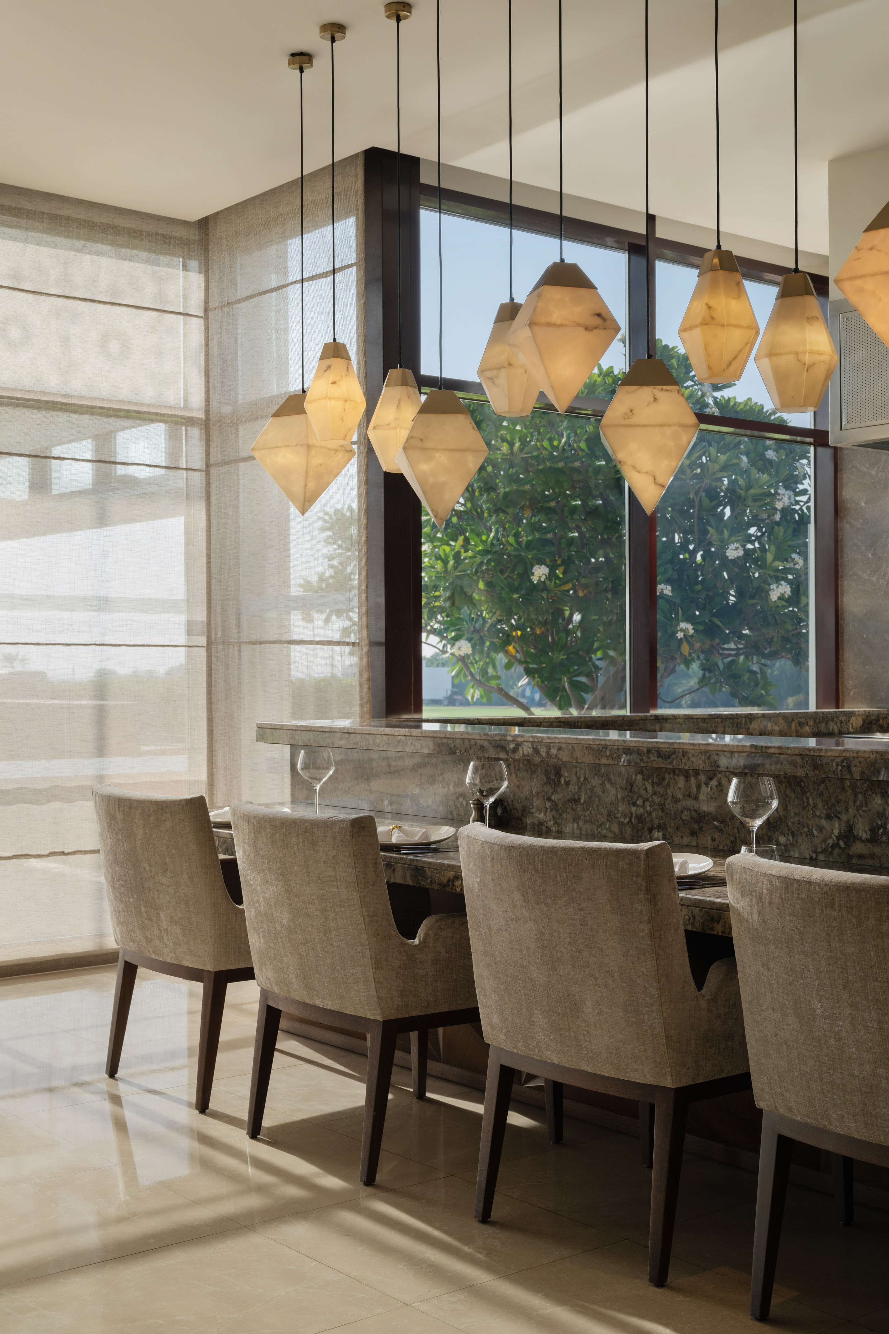 Elegant dining bar with marble counter, upholstered chairs, and unique pendant lights.