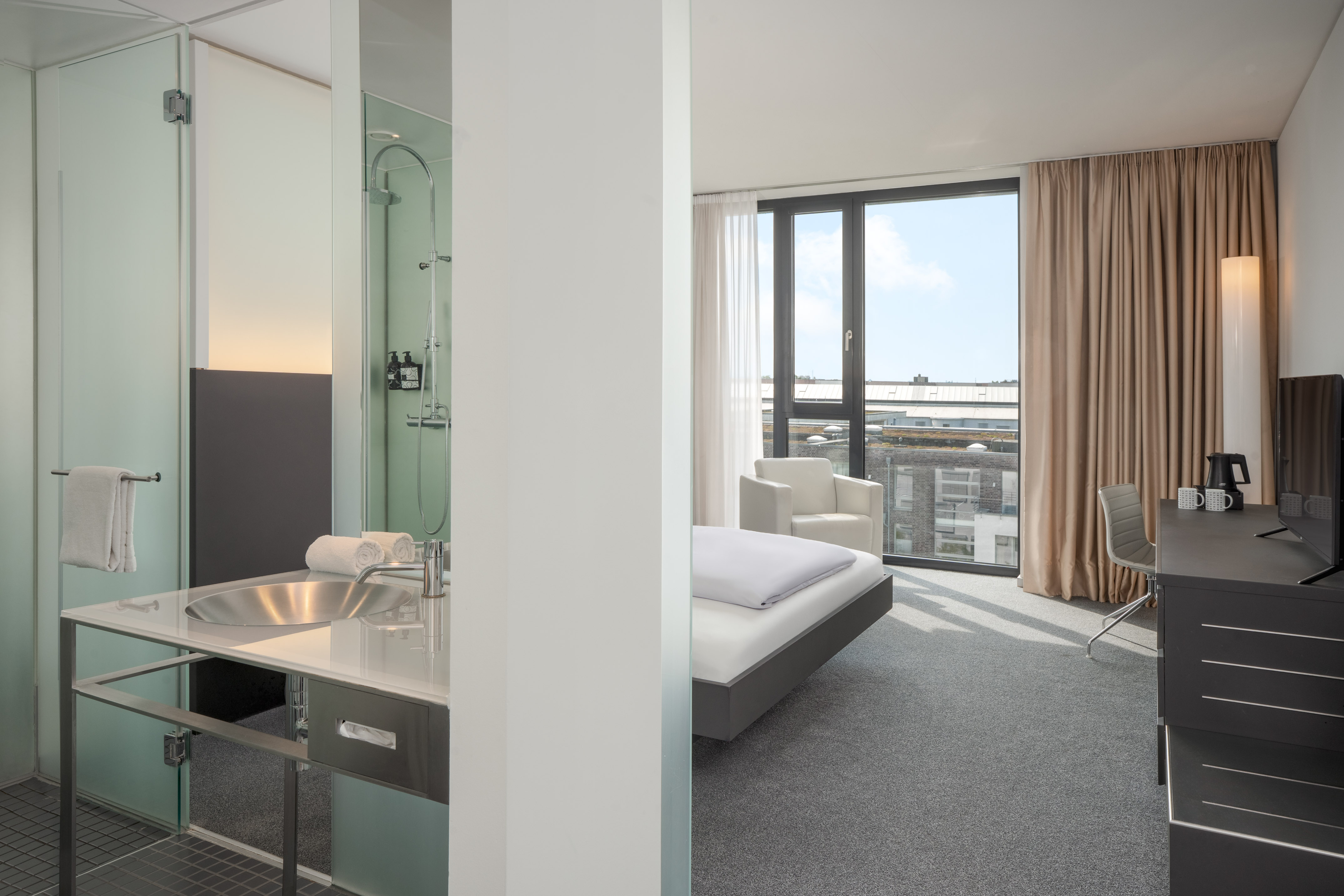 Modern hotel room with connected bathroom, bed, desk, and city view from window.