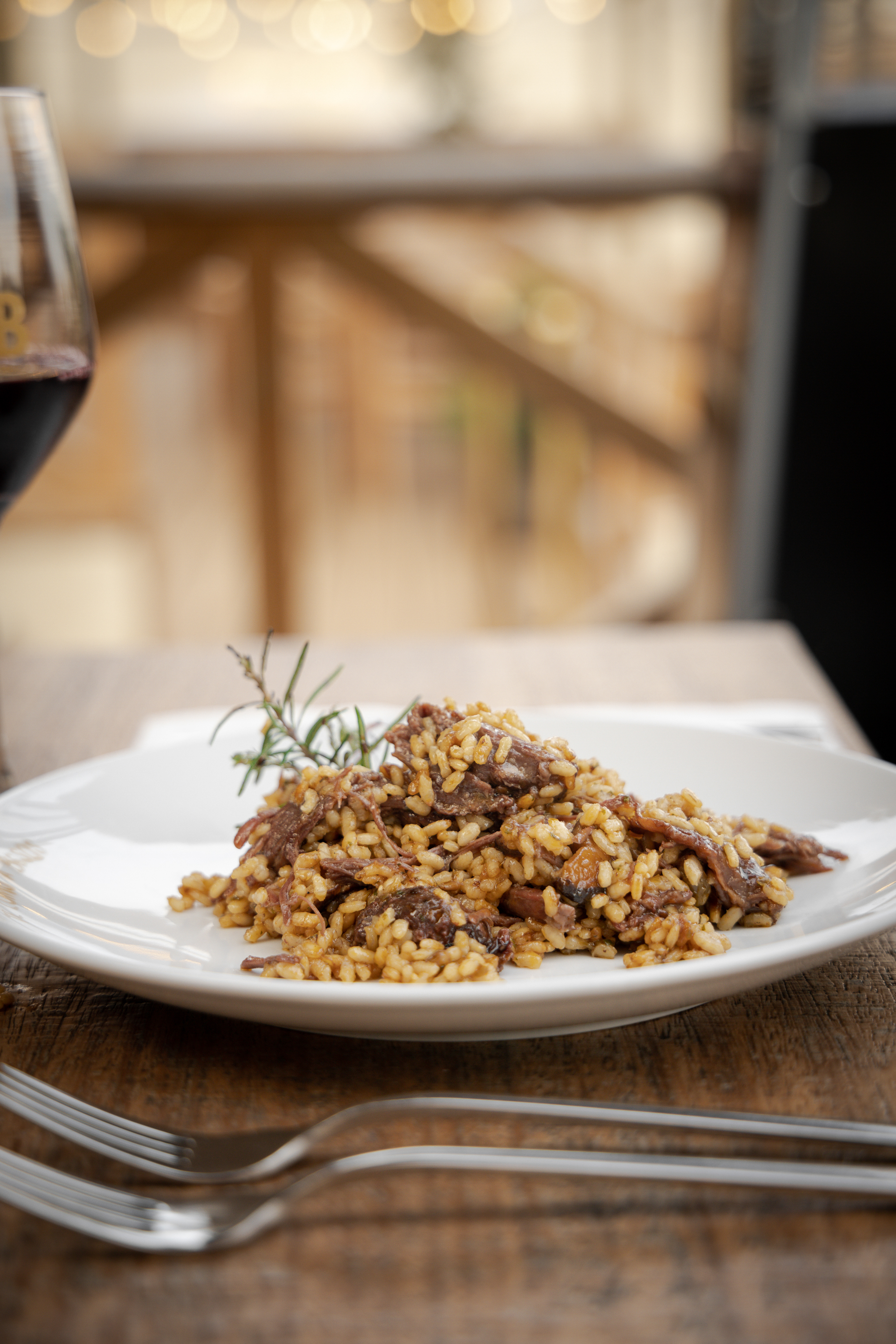 Rich meat and mushroom risotto with rosemary, white plate, red wine.