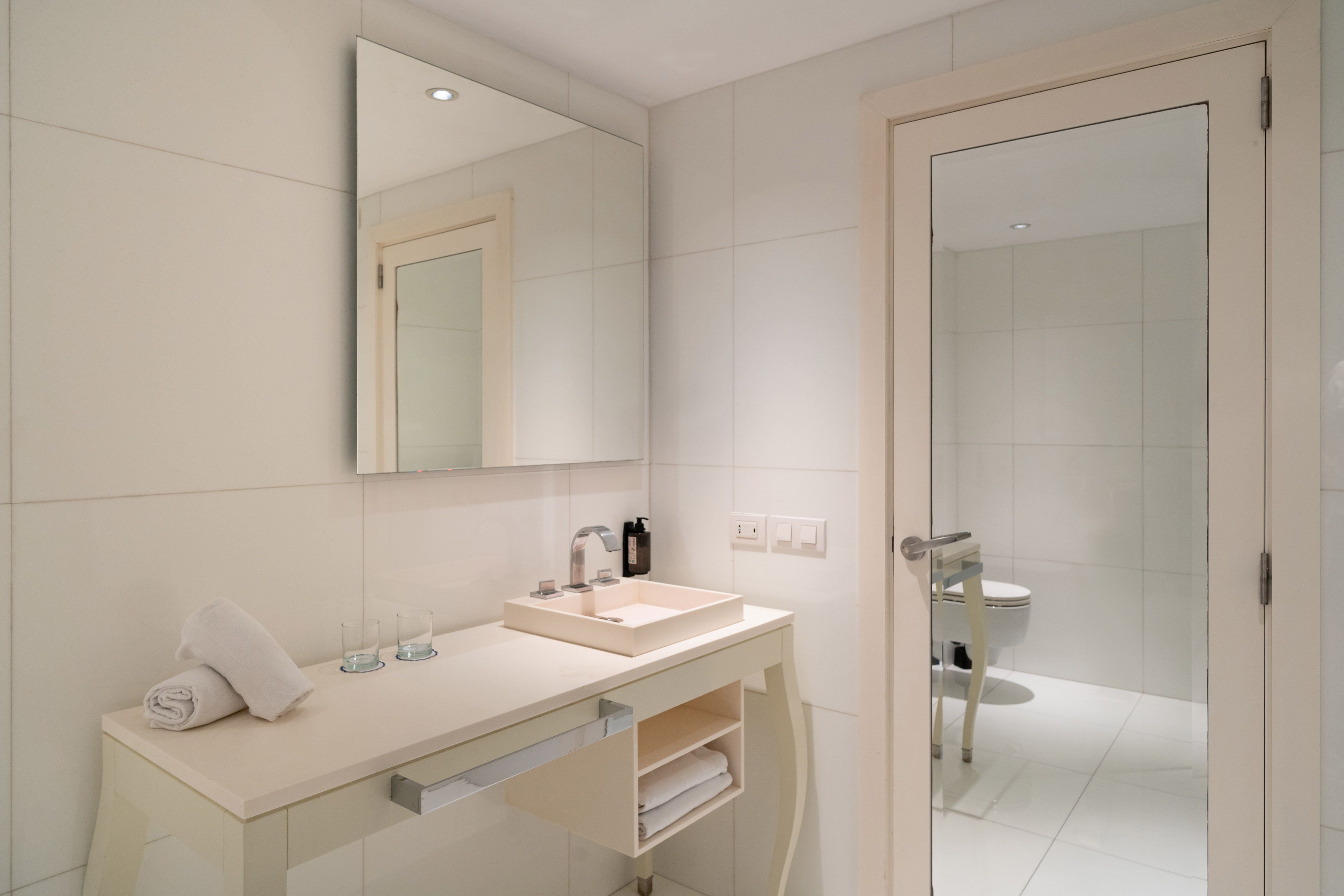 Clean modern bathroom with white vanity, sink, large mirror, and fresh towels.