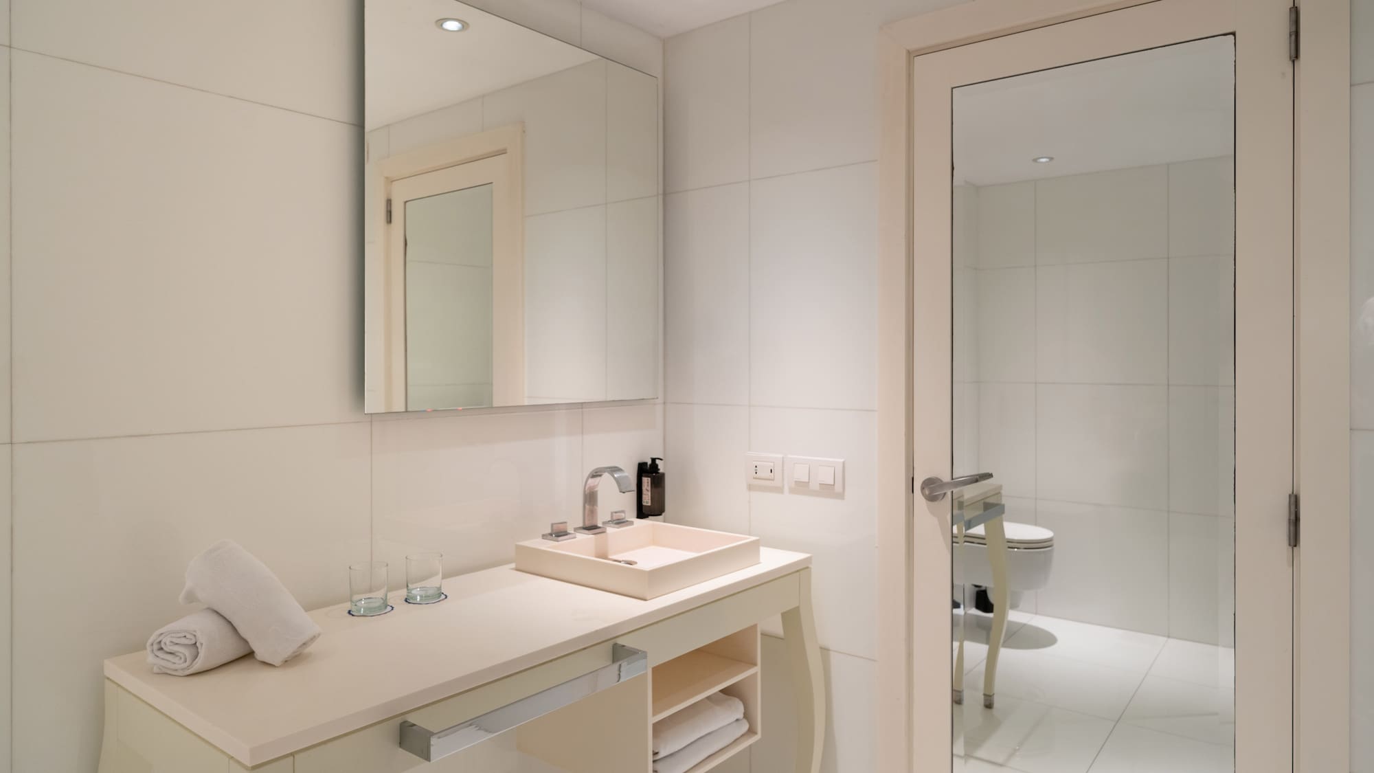 Clean modern bathroom with white vanity, sink, large mirror, and fresh towels.