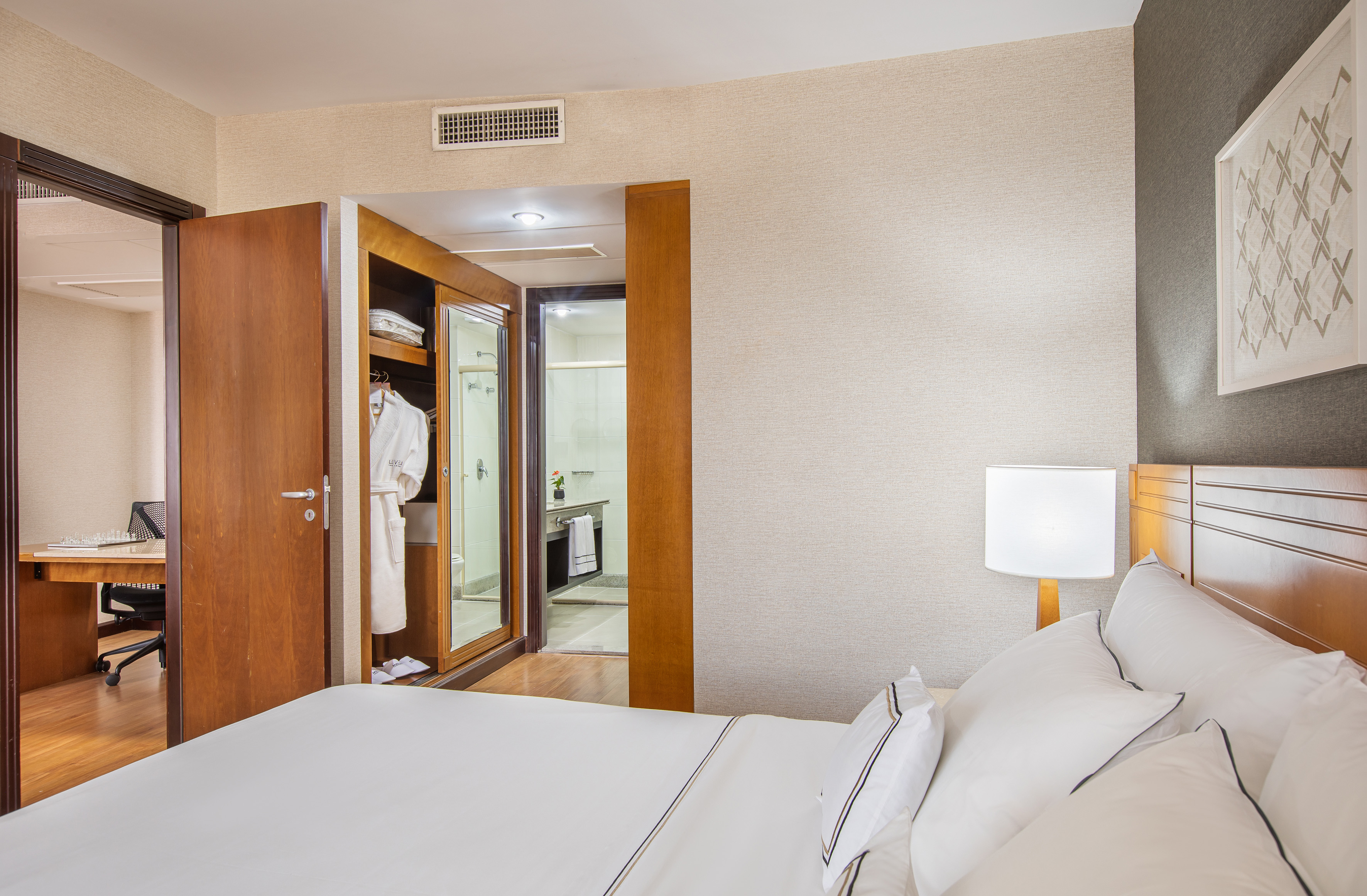 Comfortable hotel room with white bed, wooden closet, bathroom, and desk.