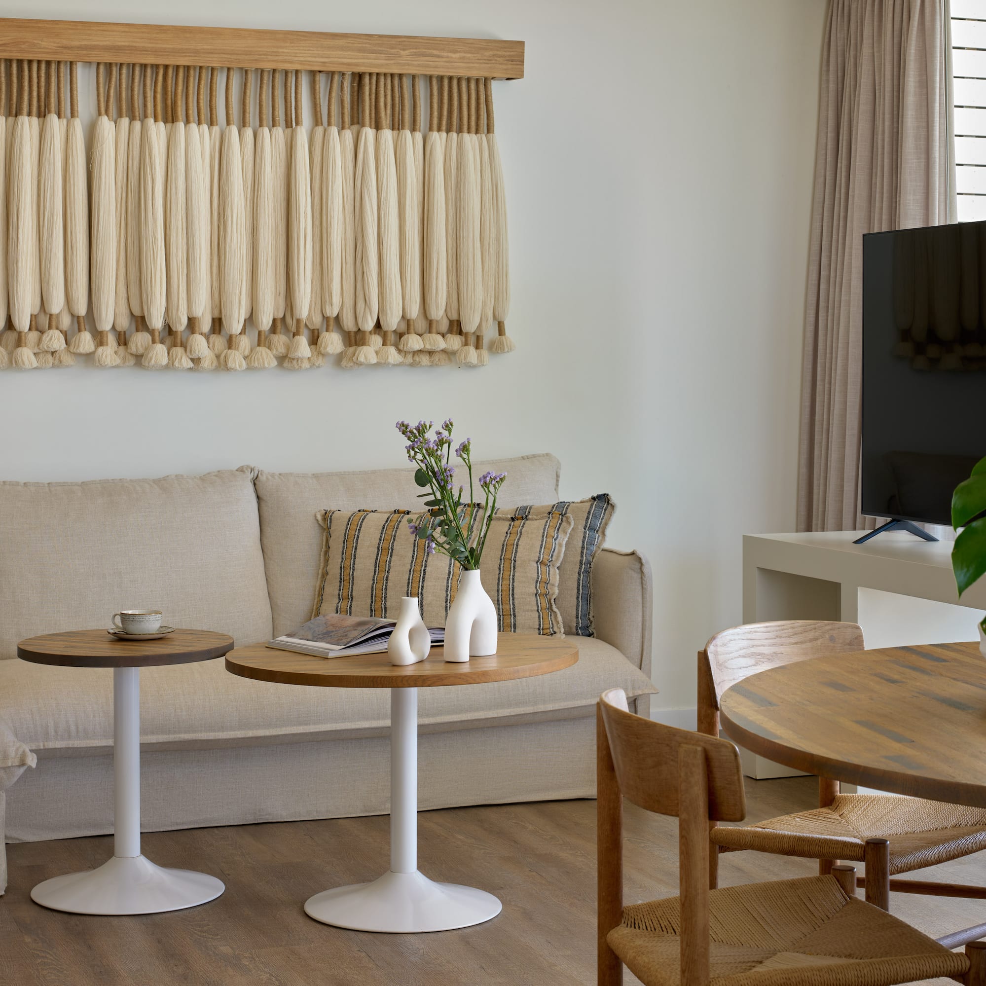 Boho living room with macrame wall art, beige sofa, and wooden dining table.