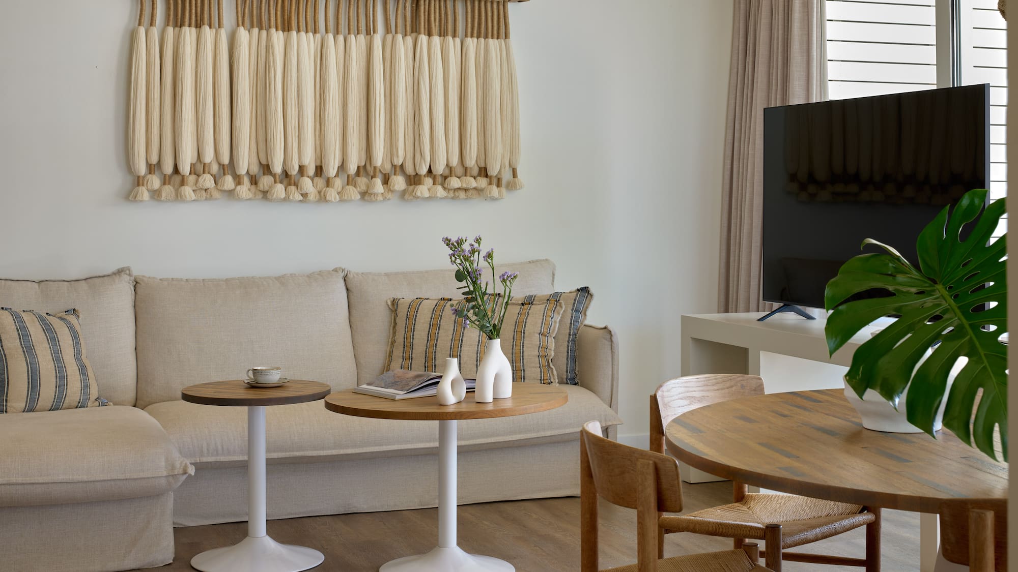 Boho living room with macrame wall art, beige sofa, and wooden dining table.