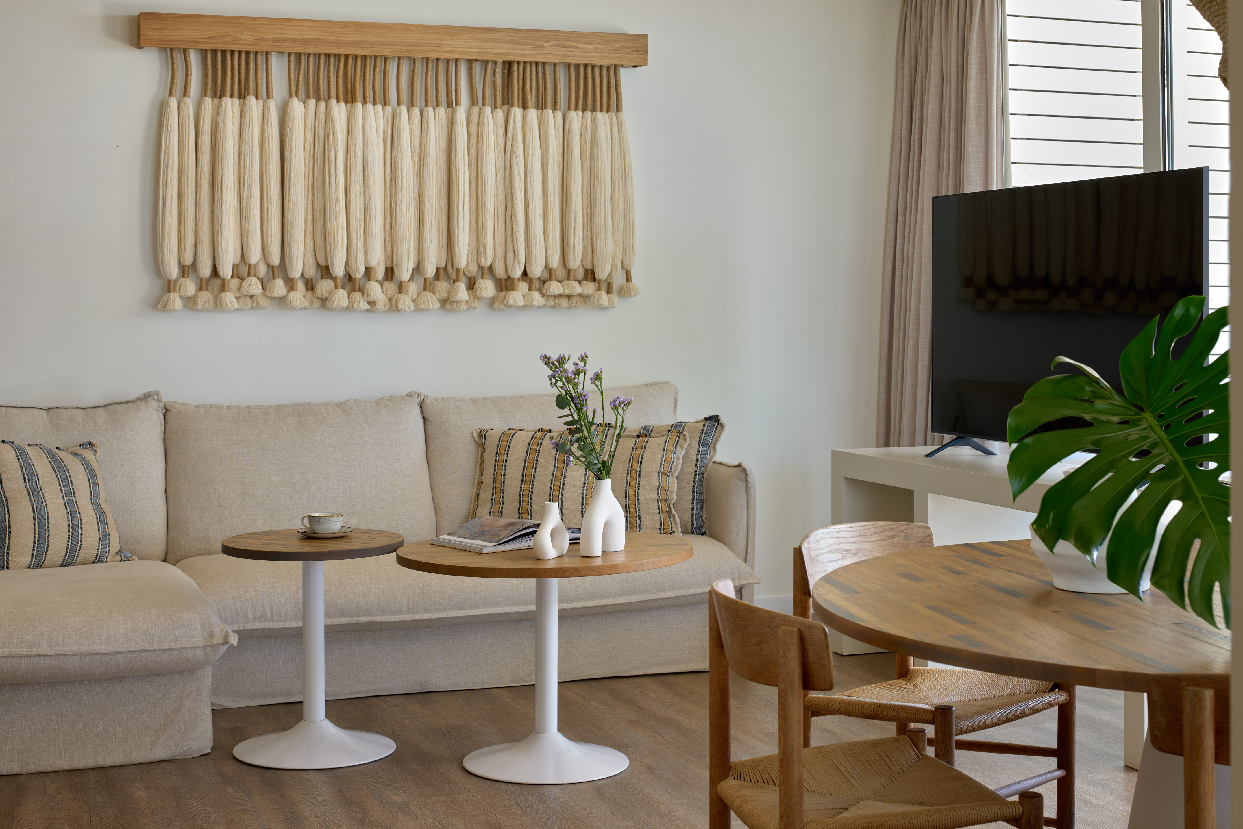 Boho living room with macrame wall art, beige sofa, and wooden dining table.