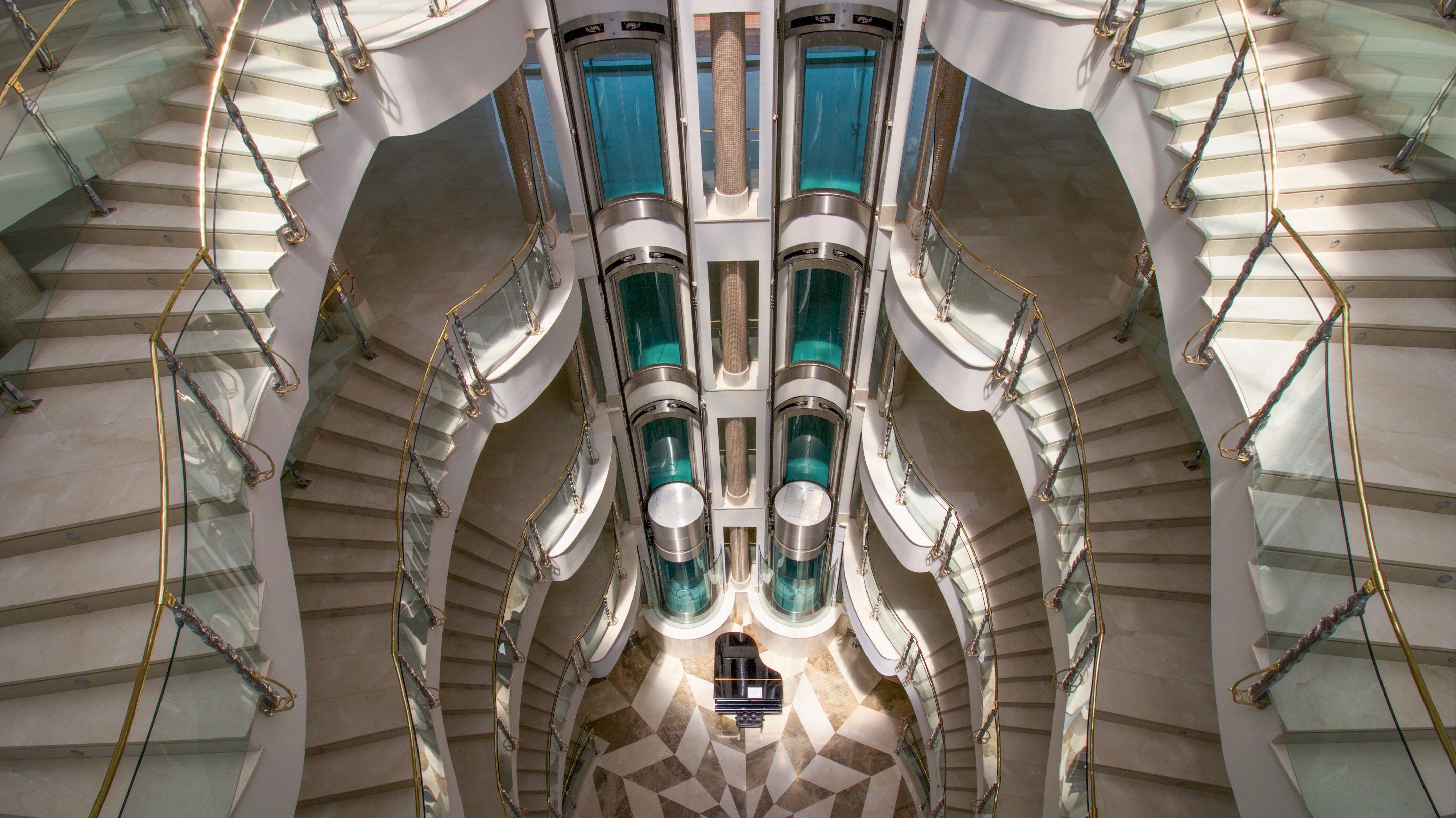 Modern atrium with marble staircases, glass elevators, grand piano.