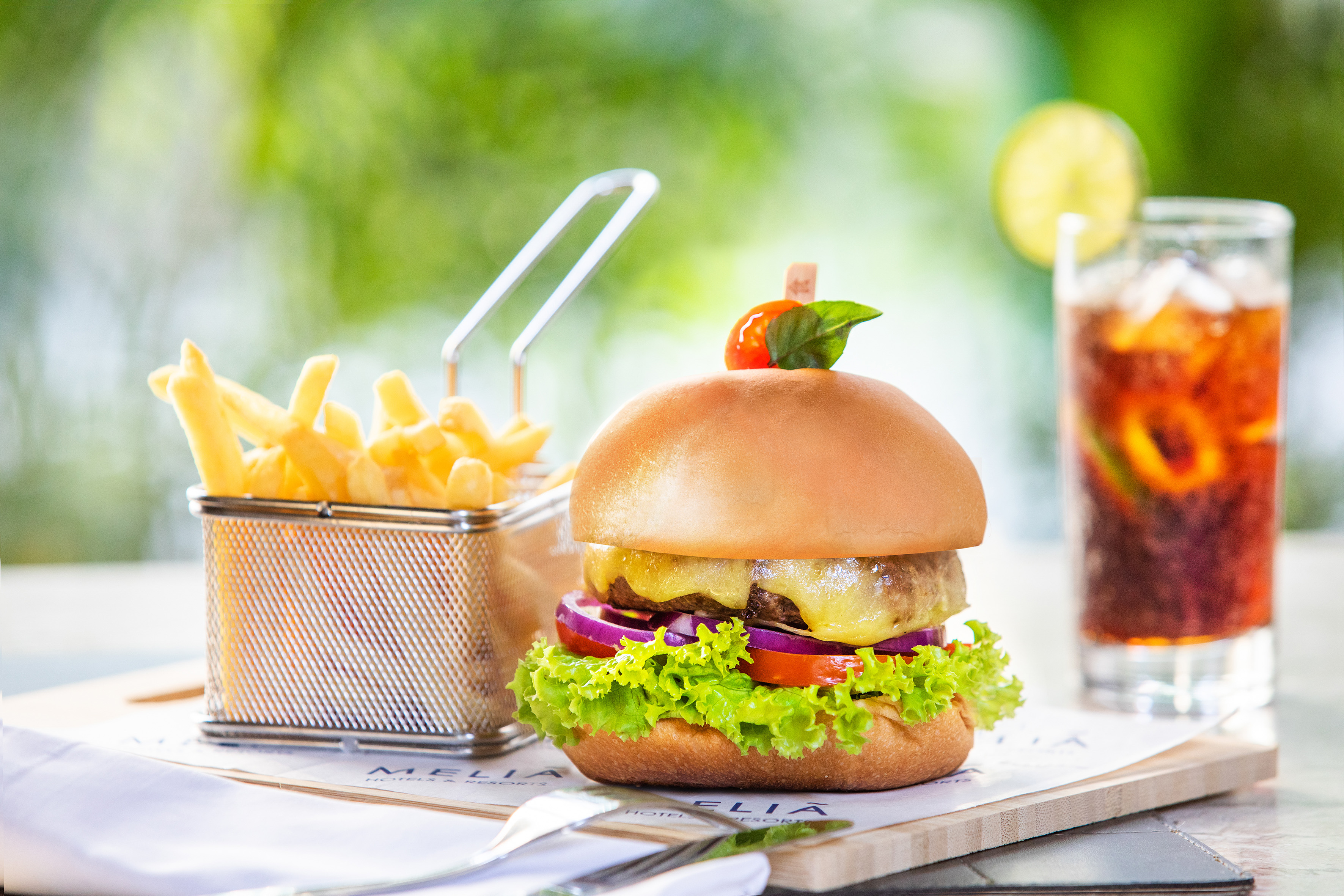 Gourmet cheeseburger with fries and cold drink at Meliá Hotels.