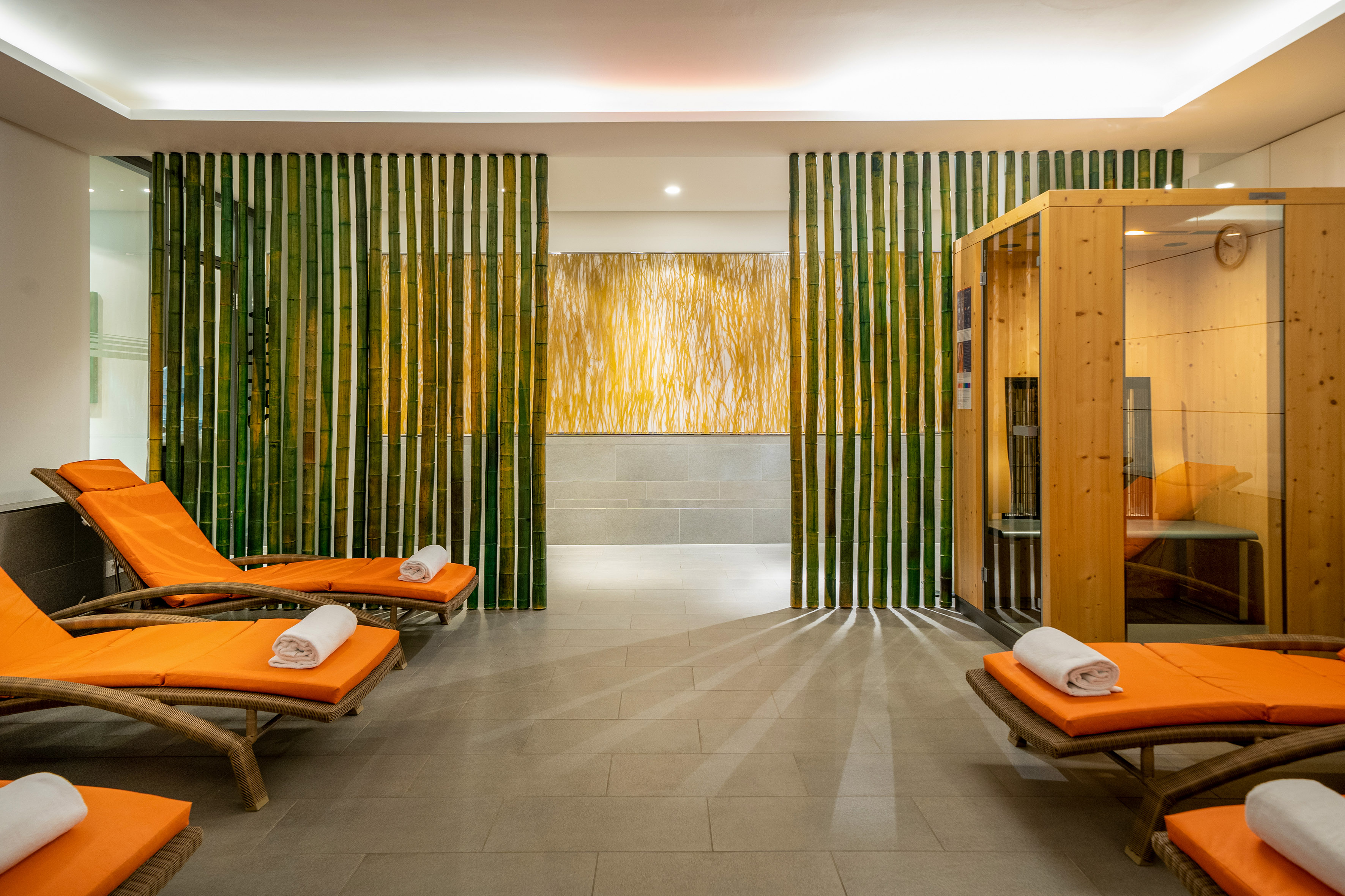 Spa relaxation area with orange lounge chairs, bamboo screen, and wooden sauna. - Înfrumusețare și spa - Innside Dresda, Dresda