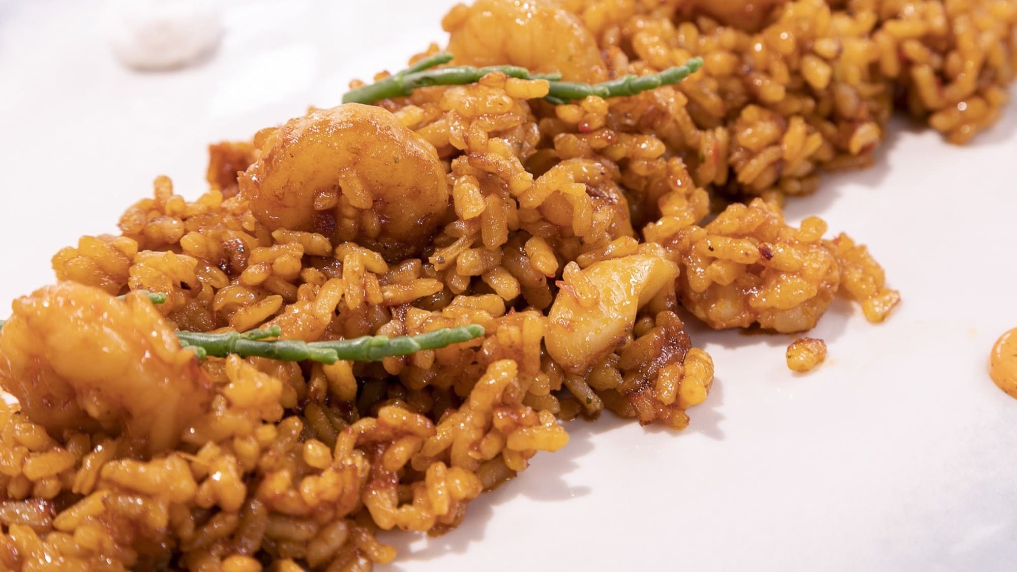Shrimp paella with green samphire on white plate, close-up.