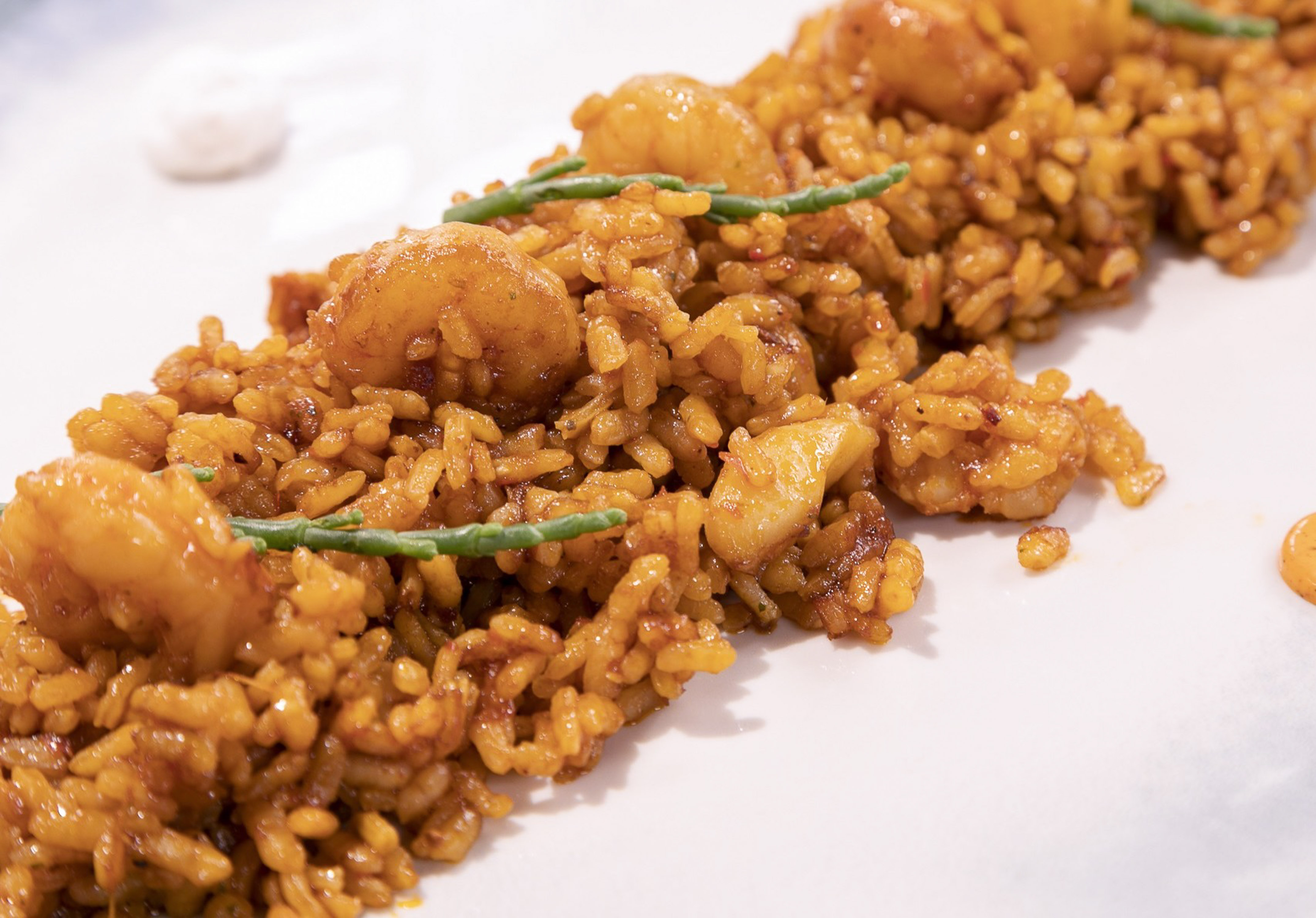 Shrimp paella with green samphire on white plate, close-up.