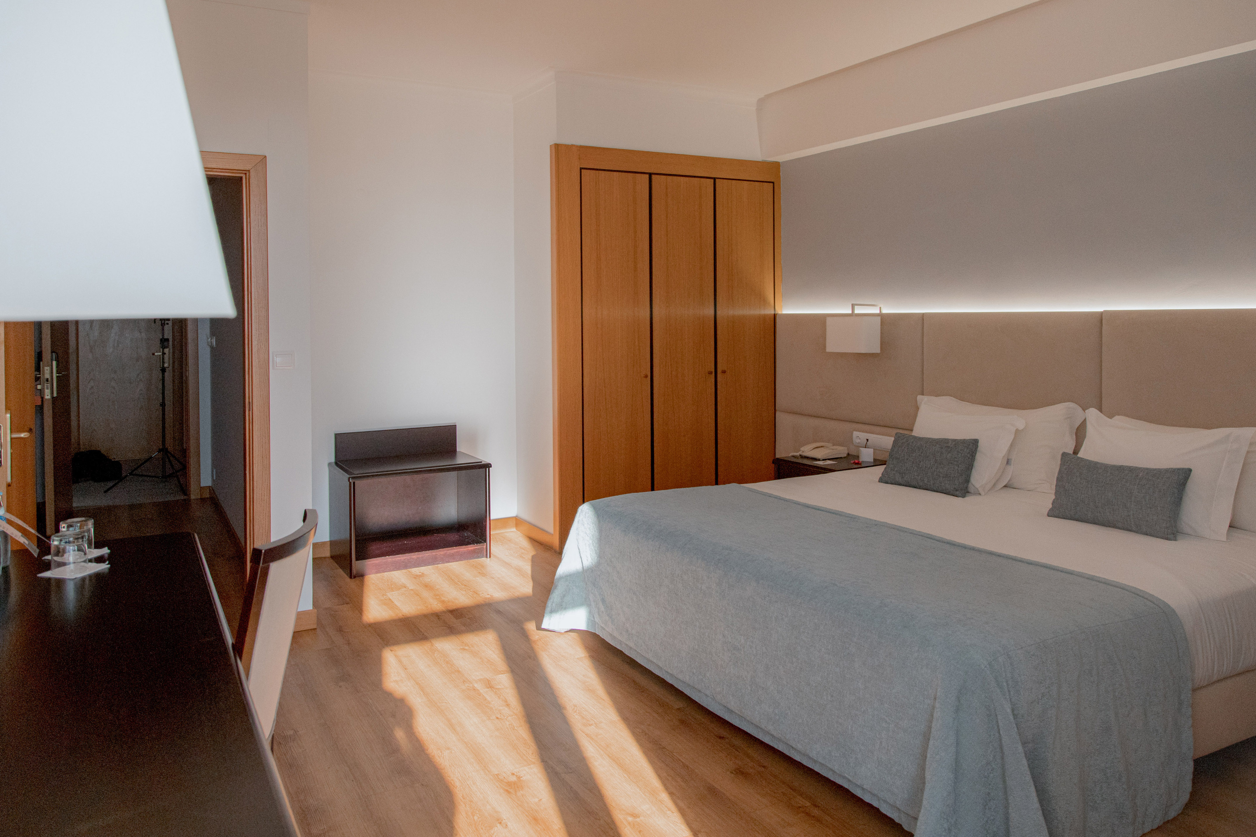 Modern hotel room interior with bed, light blue throw, wooden wardrobe, and floor.