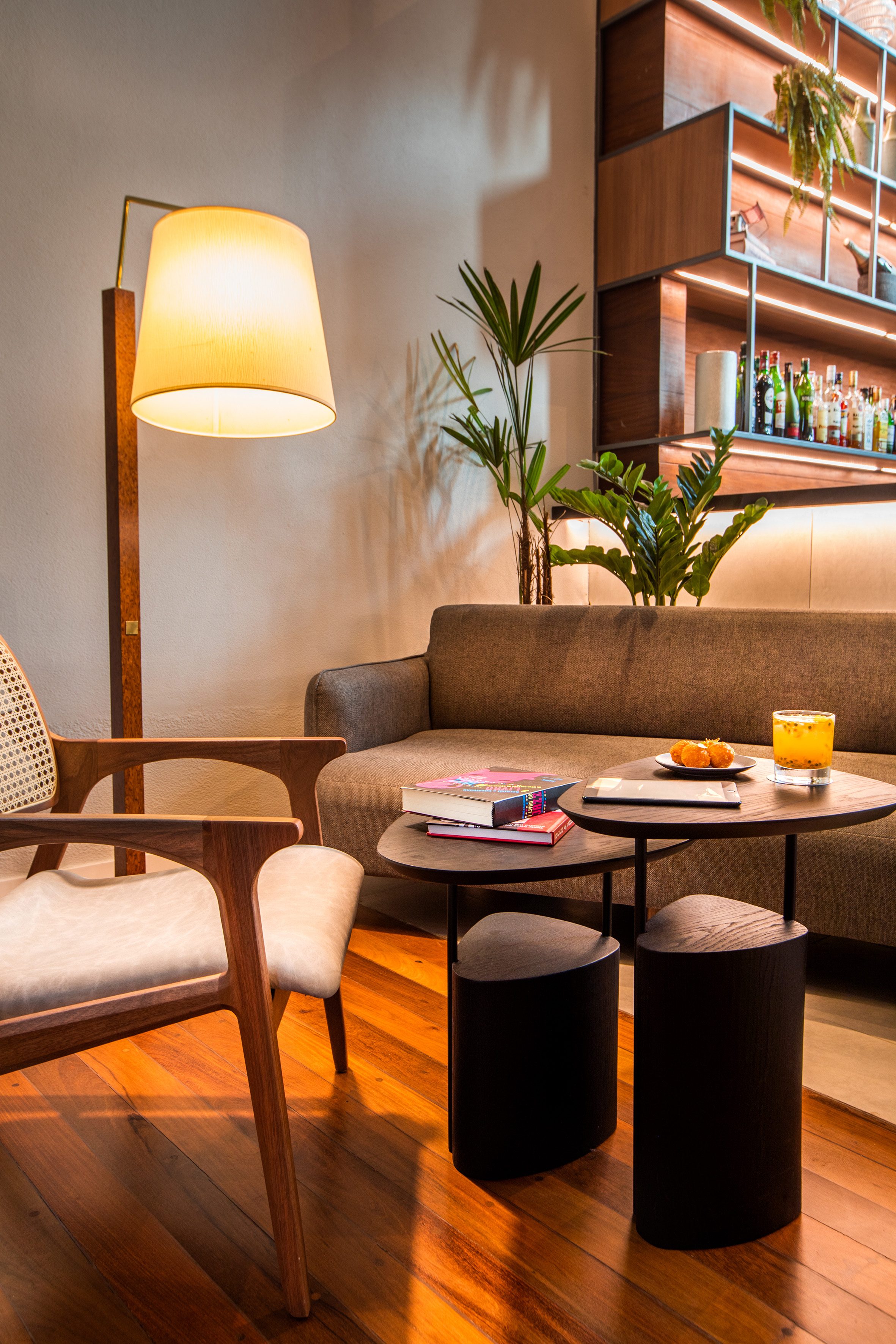 Cozy lounge with wooden armchair, sofa, coffee tables, and illuminated bar.