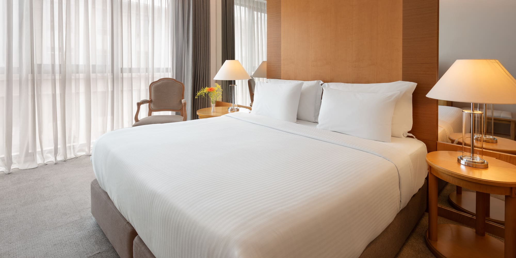 Modern hotel room with king bed, white sheets, wooden headboard, and lamps.