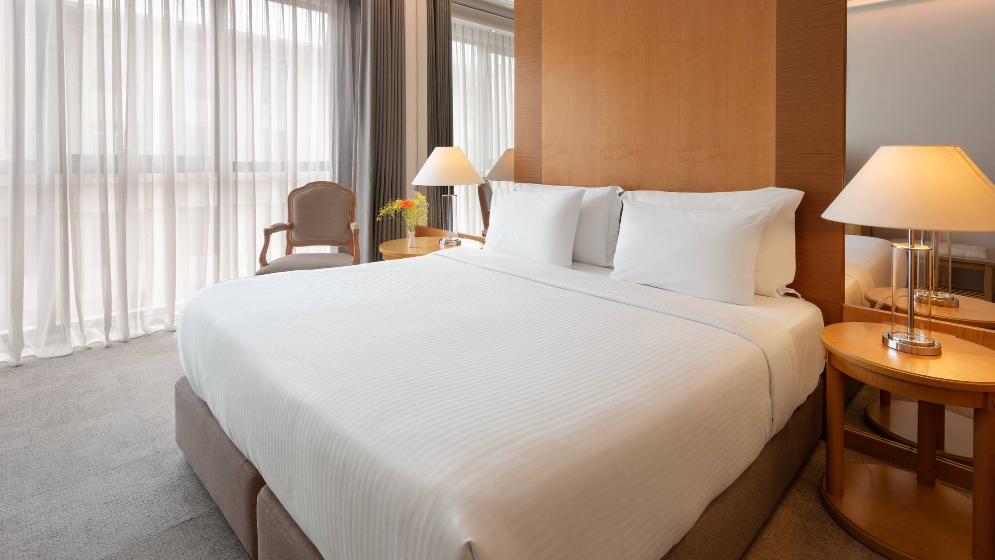 Modern hotel room with king bed, white sheets, wooden headboard, and lamps.