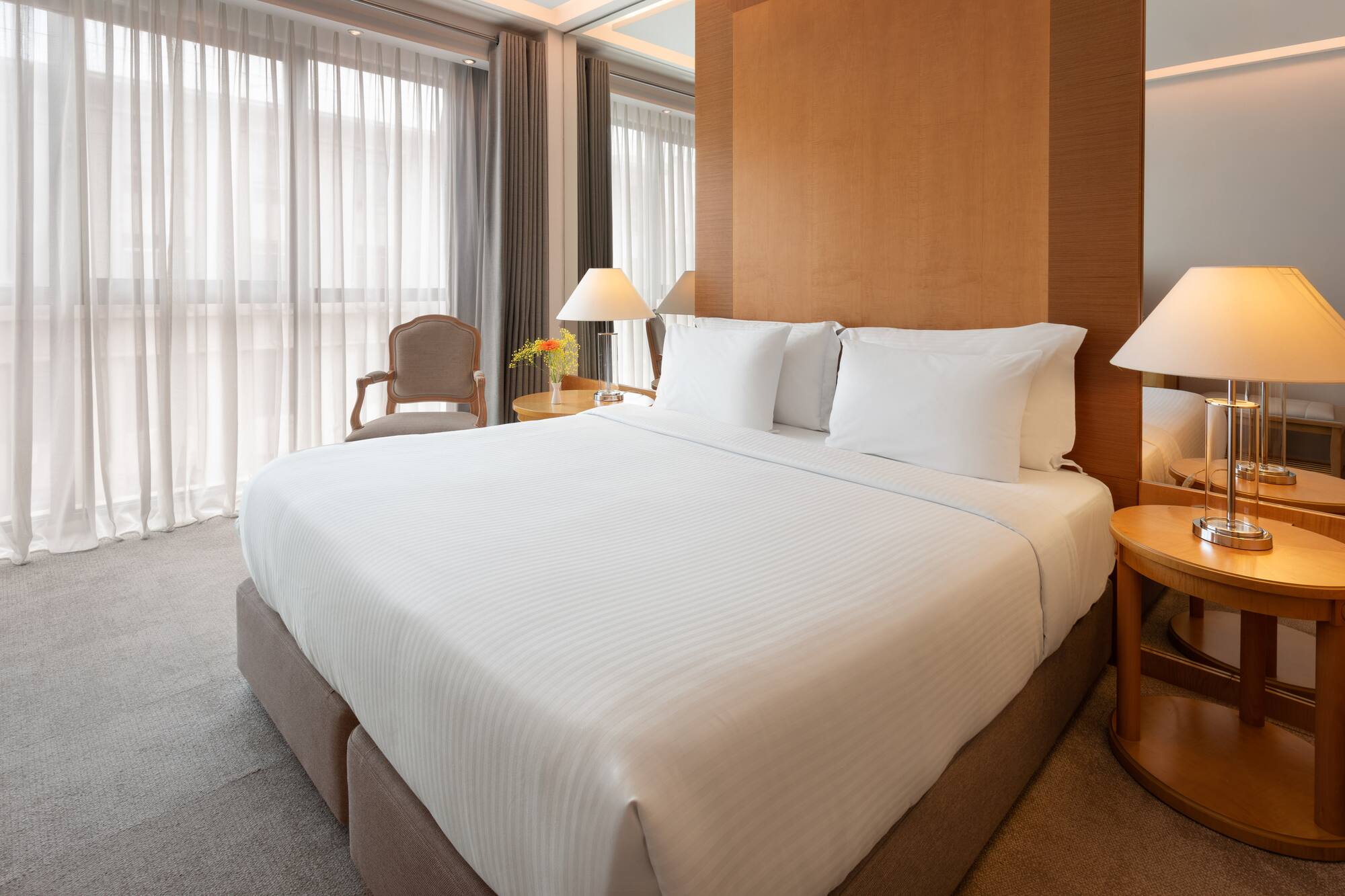 Modern hotel room with king bed, white sheets, wooden headboard, and lamps.