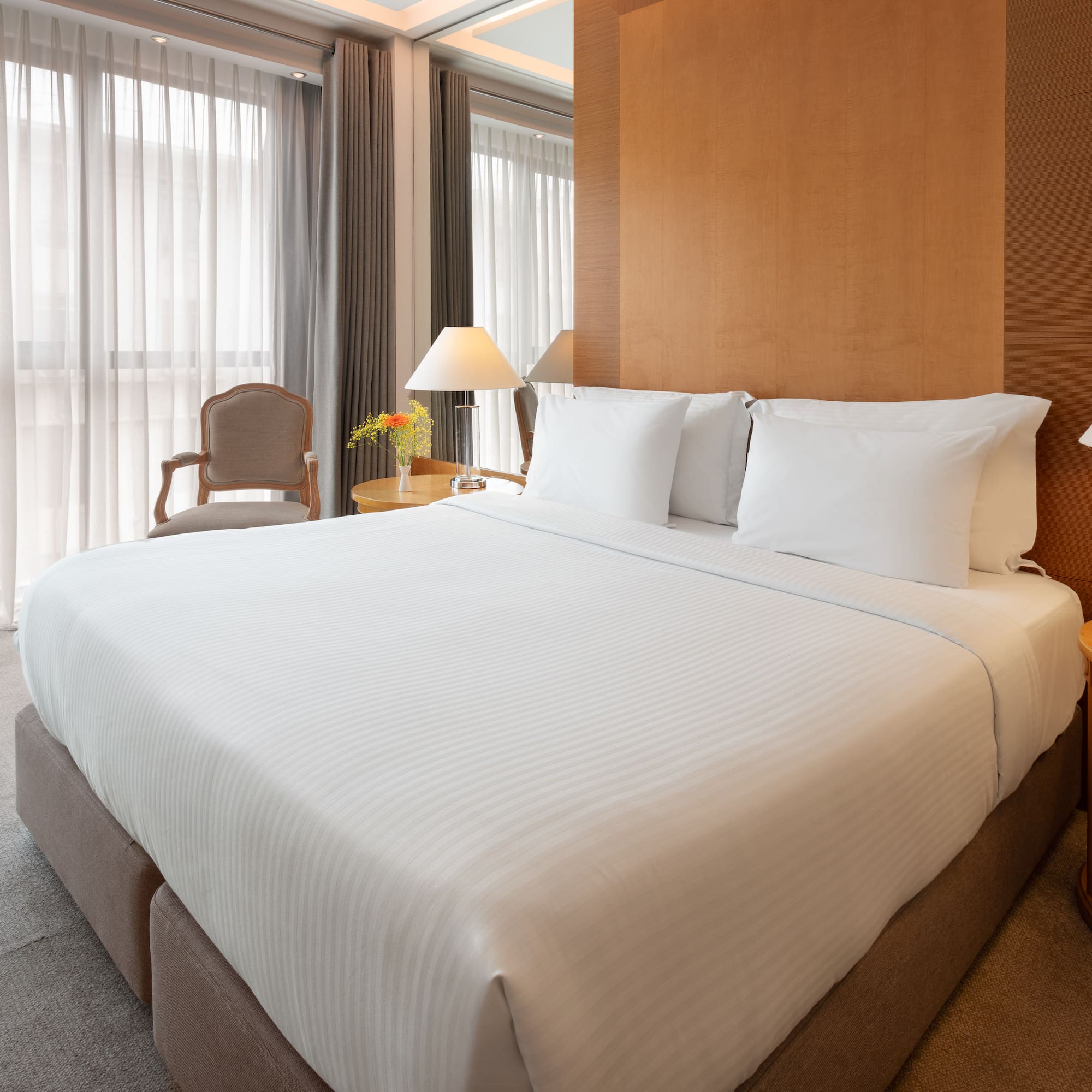 Modern hotel room with king bed, white sheets, wooden headboard, and lamps.