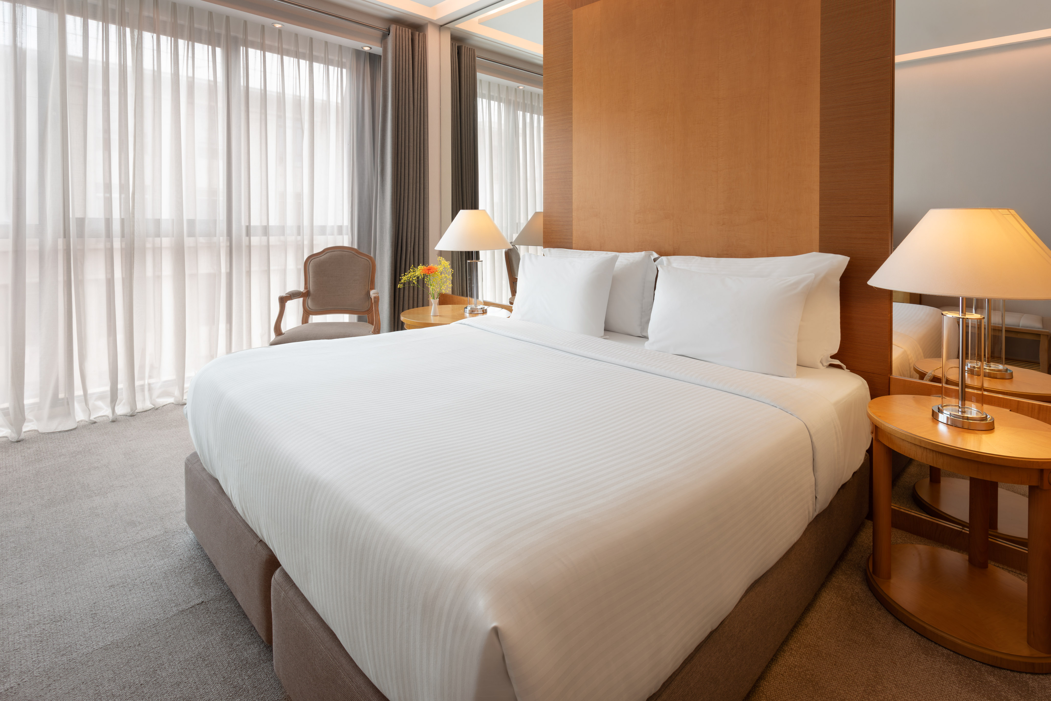 Modern hotel room with king bed, white sheets, wooden headboard, and lamps.