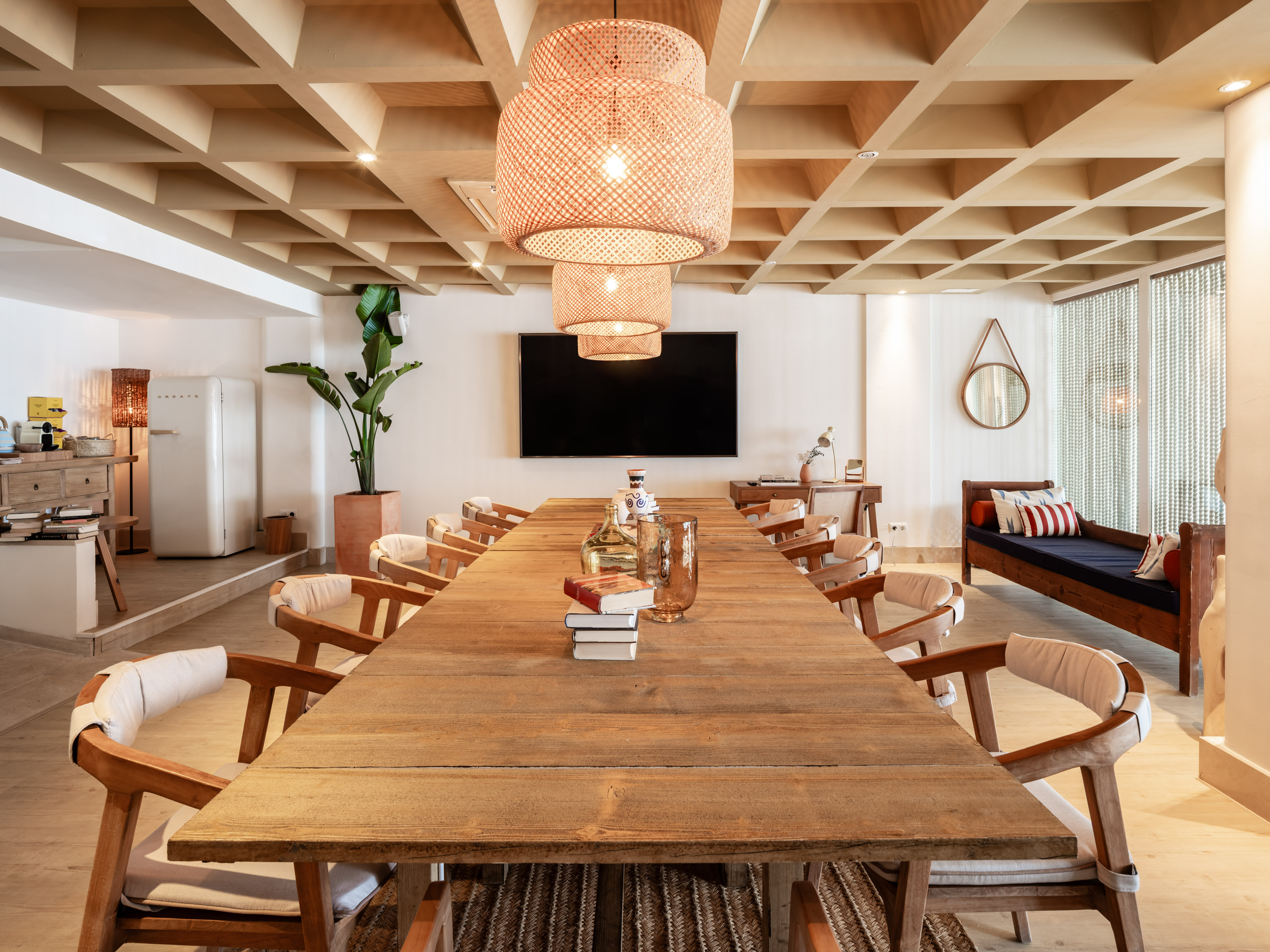 Bohemian meeting room with long rustic wooden table and rattan pendant lights.
