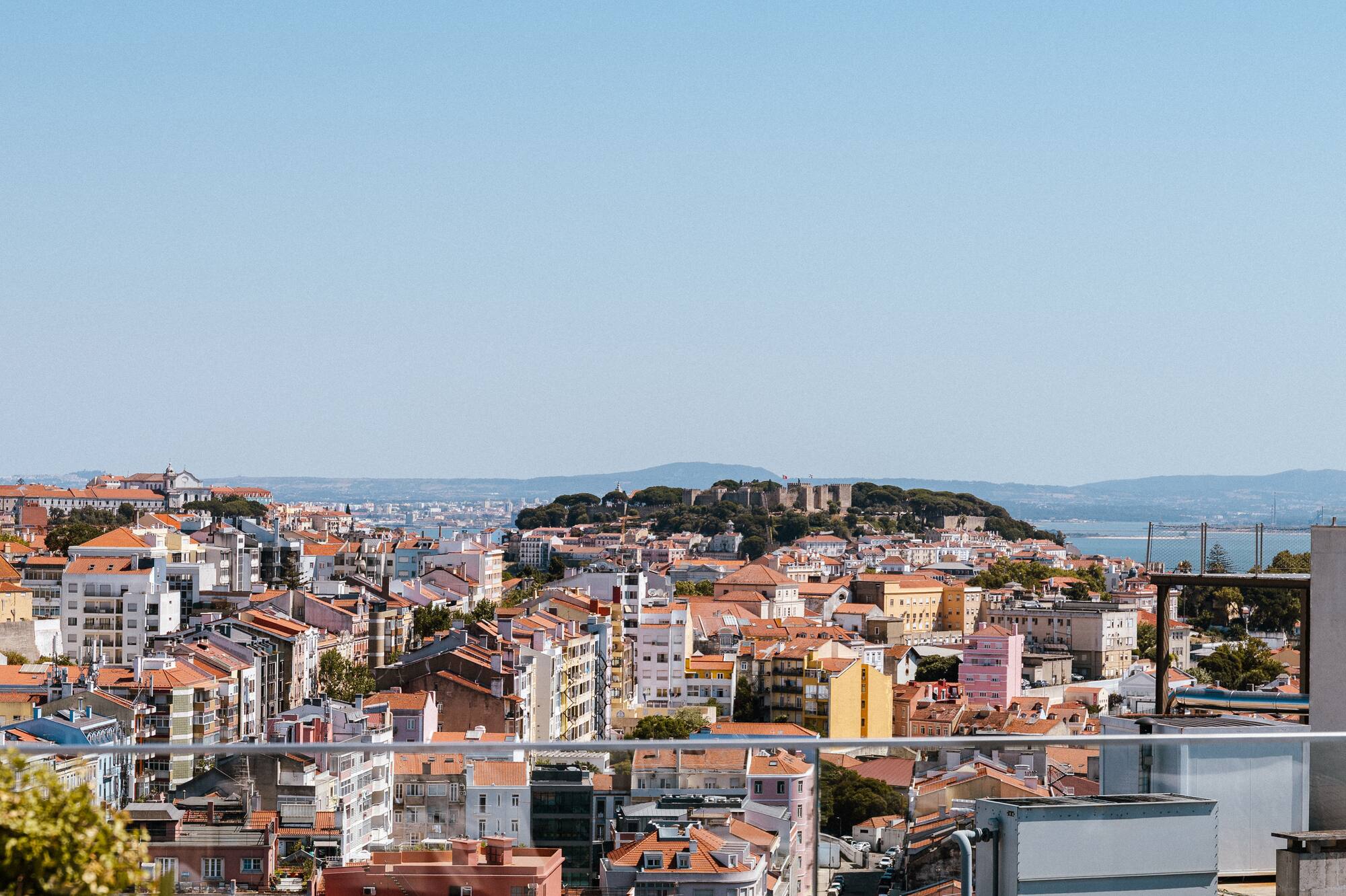Lisbon cityscape from rooftop terrace with São Jorge Castle and Tagus River.