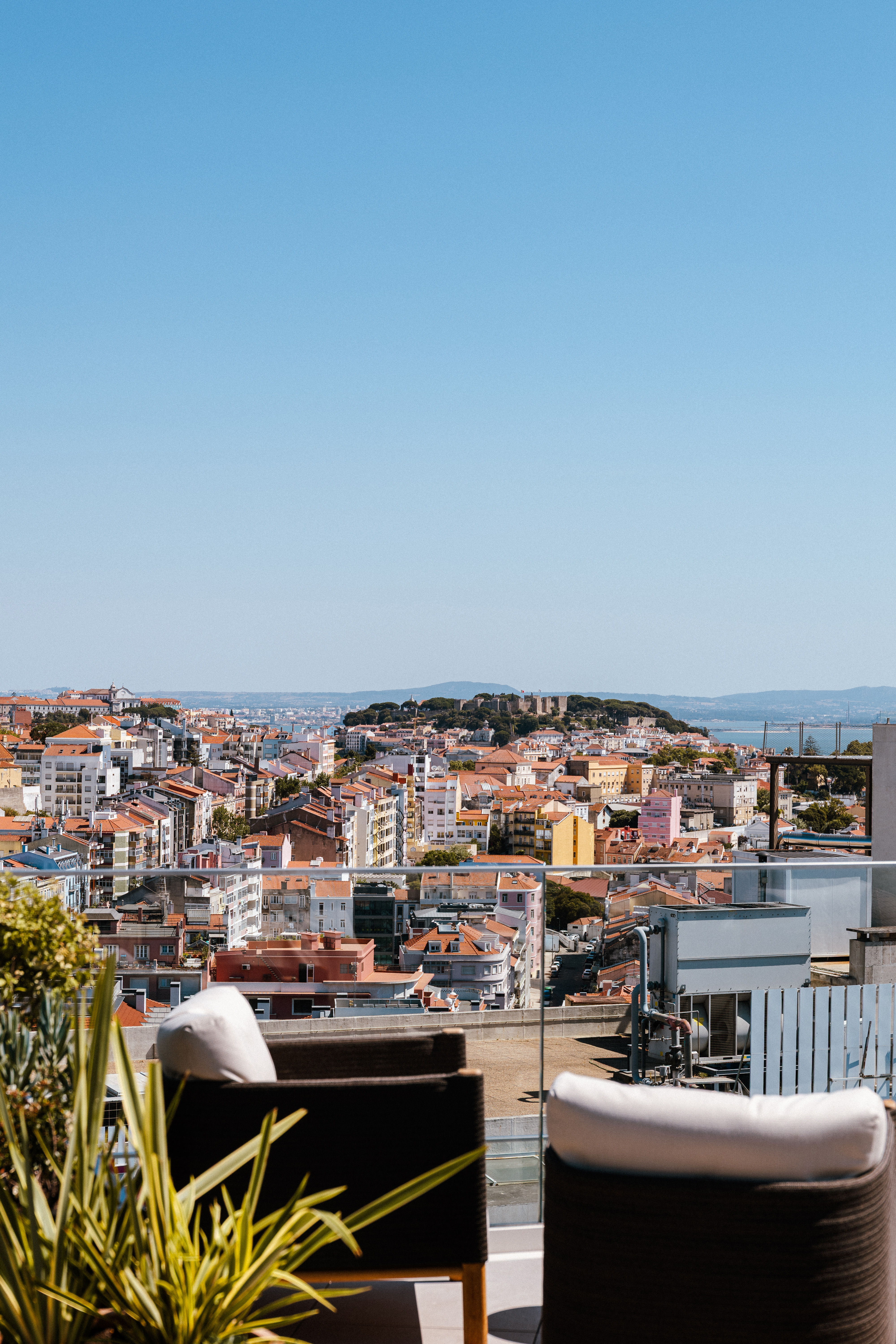 Lisbon cityscape from rooftop terrace with São Jorge Castle and Tagus River.